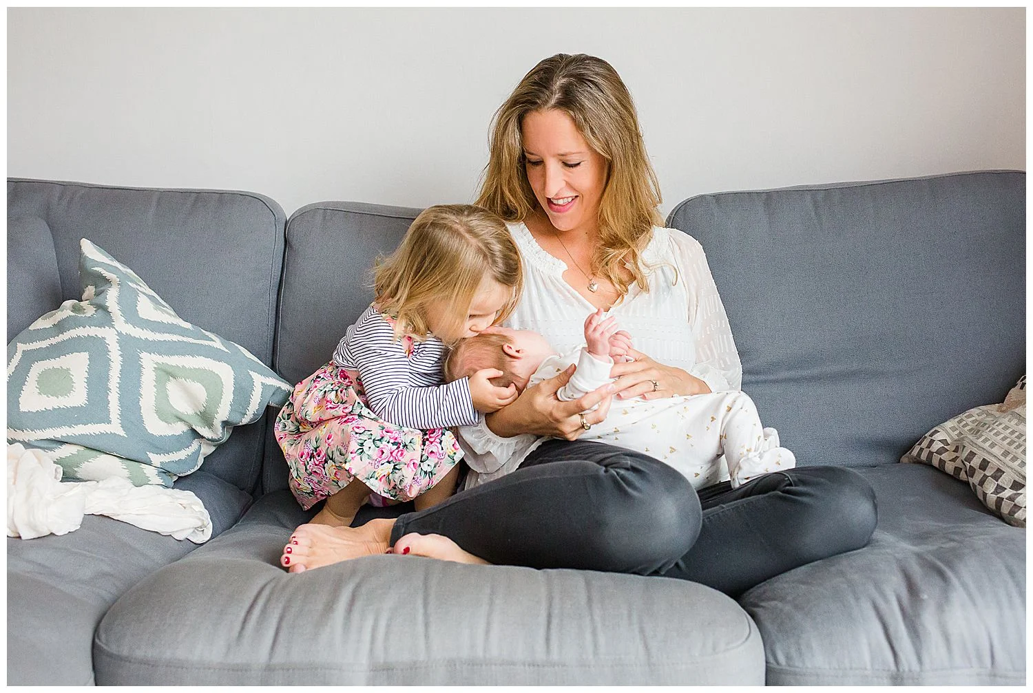 toddler kissing newborn baby in mum's lap
