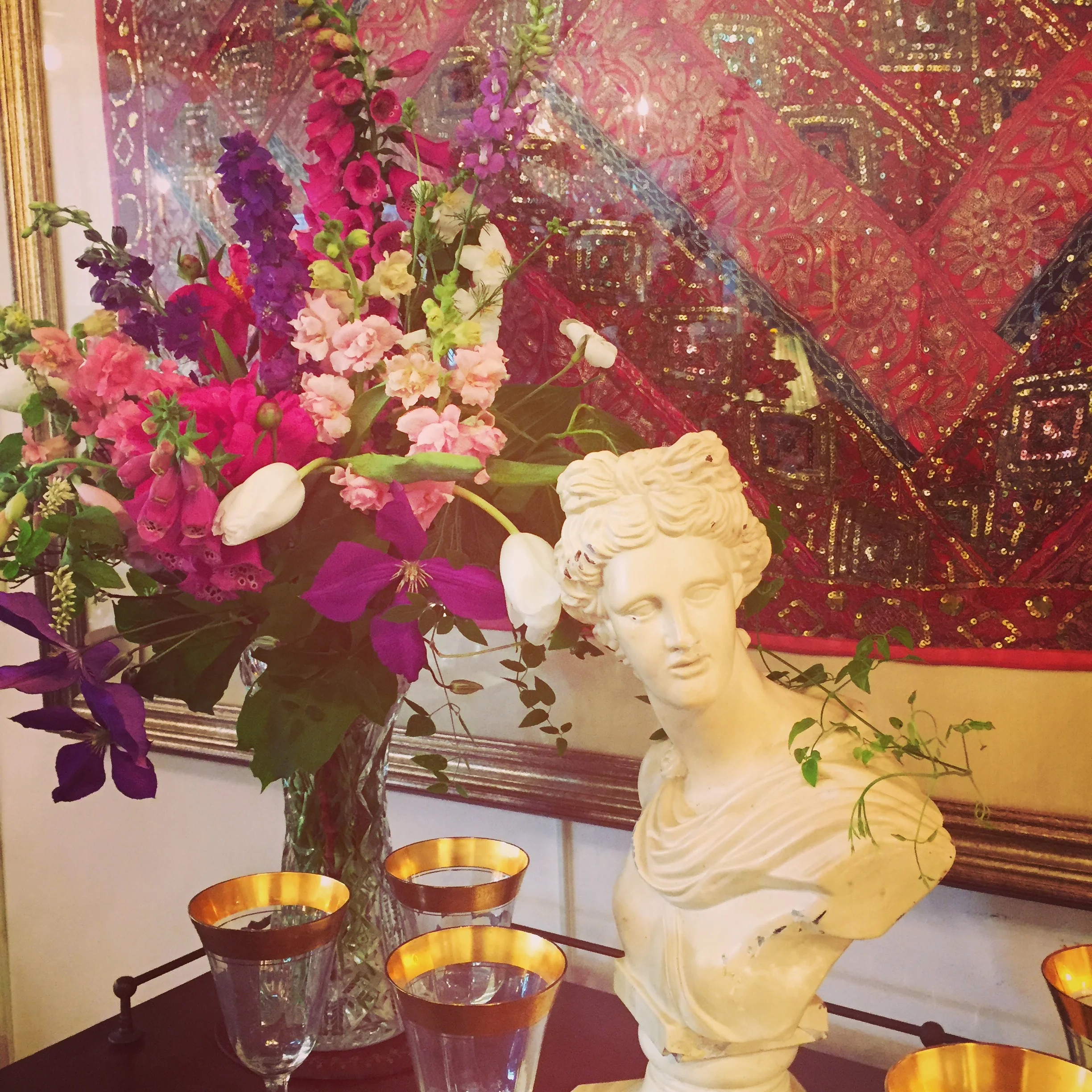 Early summer flowers including fox glove, sweet pea and clematis with a grecian bust and stemware at Goldsborough Glynn Antiques