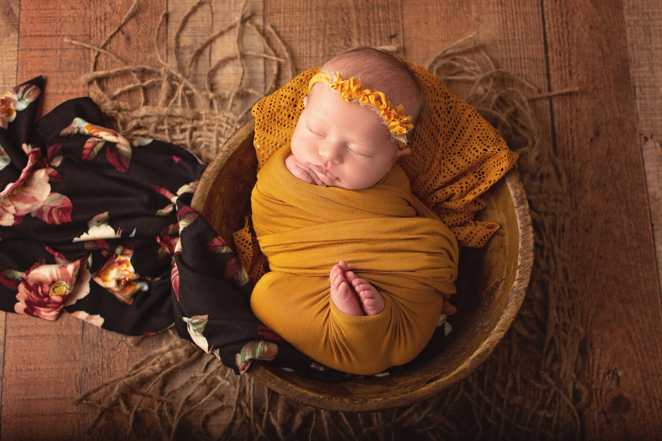 Newborn baby girl in yellow wrap wooden bowl