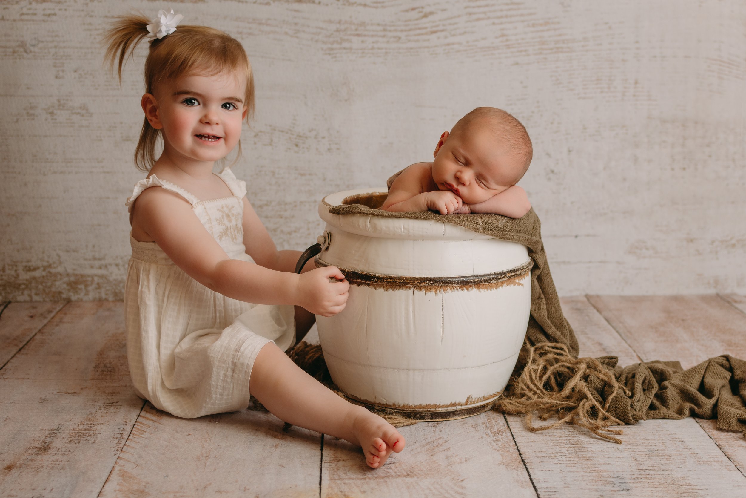 Big sister next to newborn baby in a bucket
