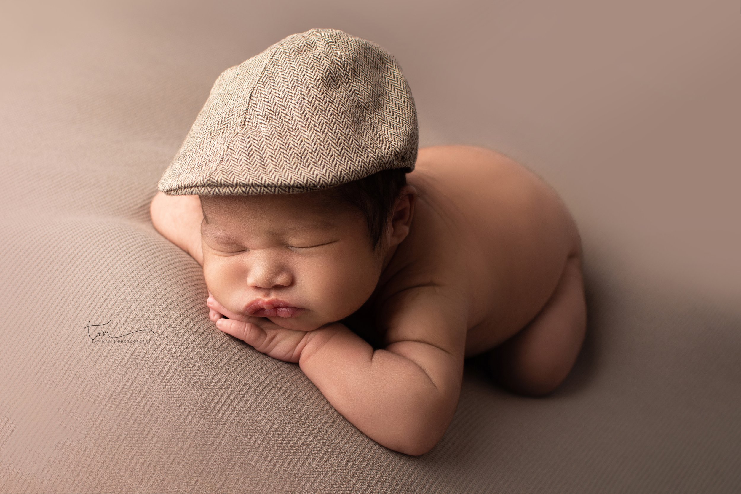 newborn baby boy in hat hands under chin