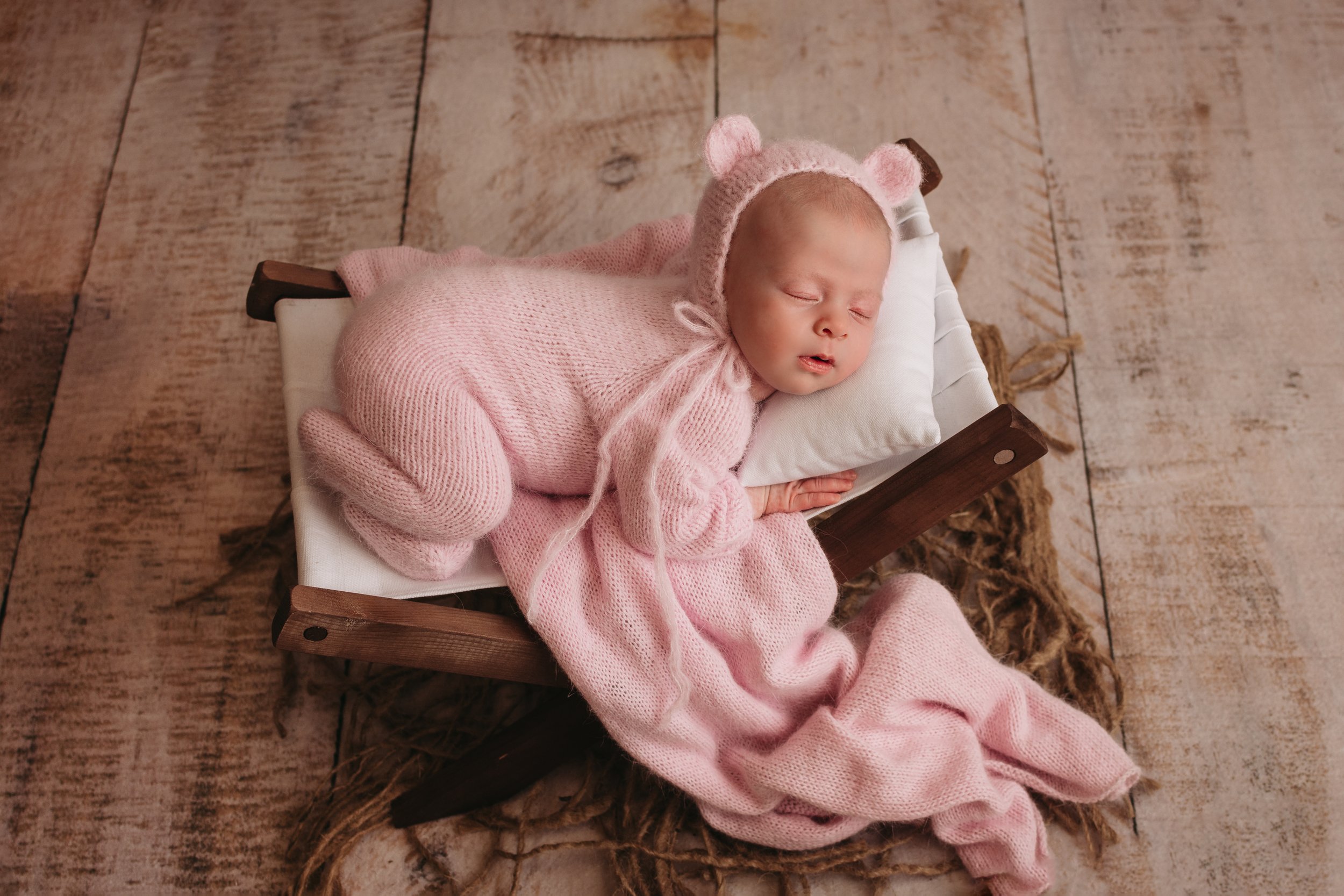 Newborn baby girl in pink furry bear outfit laying on little bed
