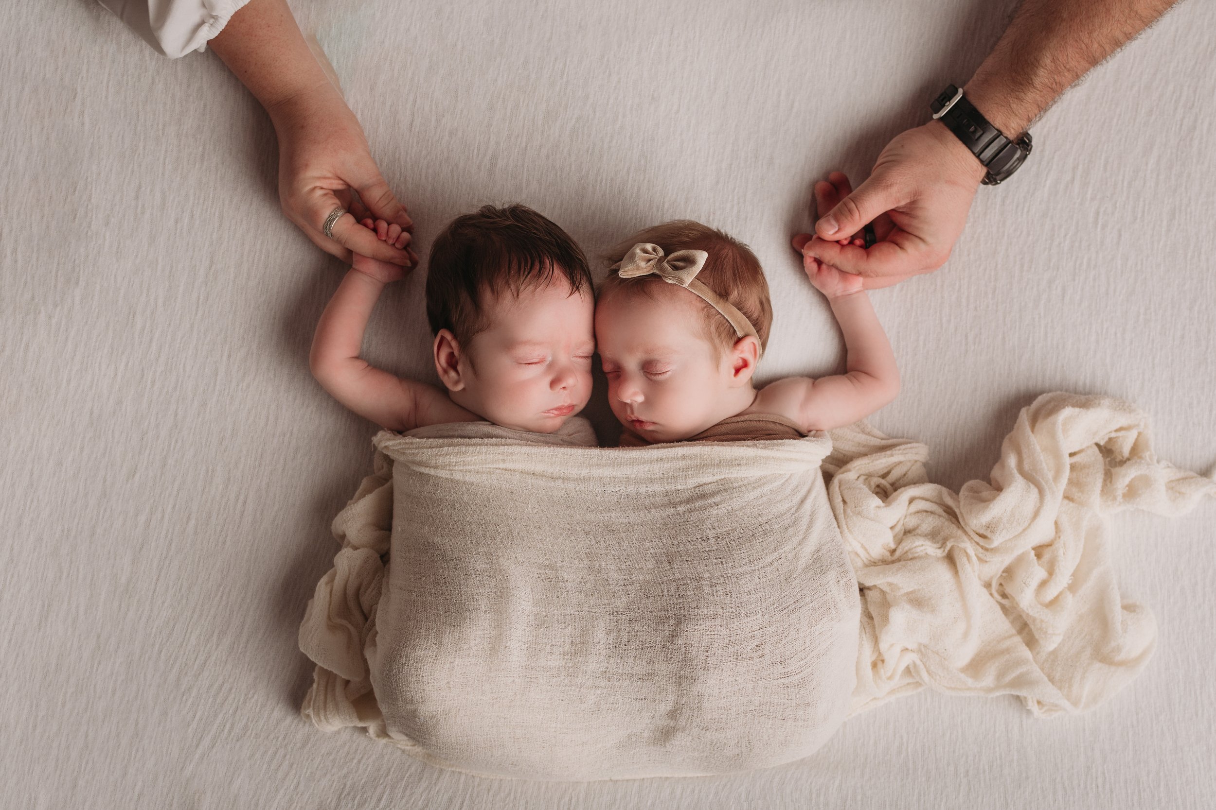 Newborn twins holding parents hands