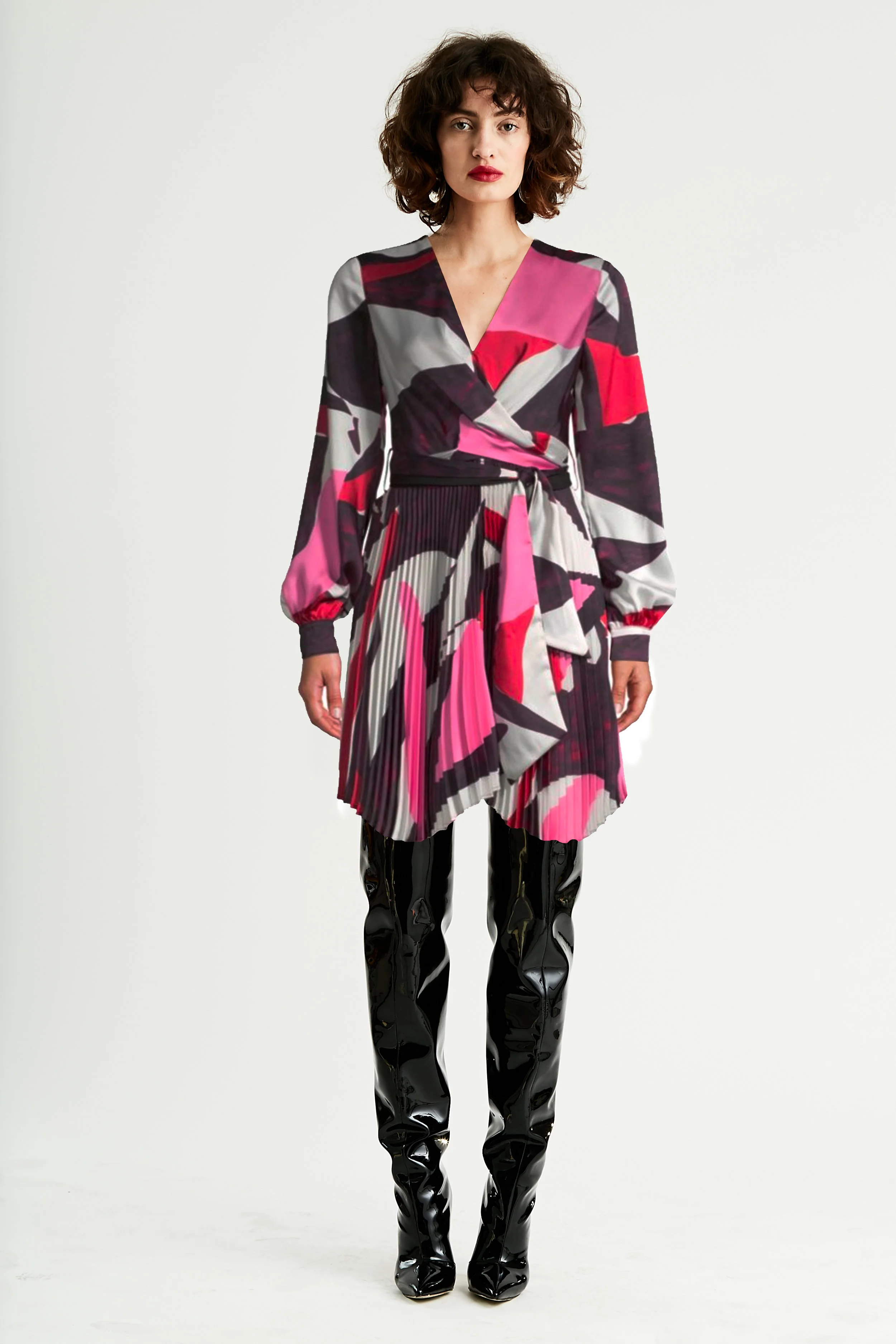 Model stands in long sleeve short dress in abstract collage print with black thigh high patent boots