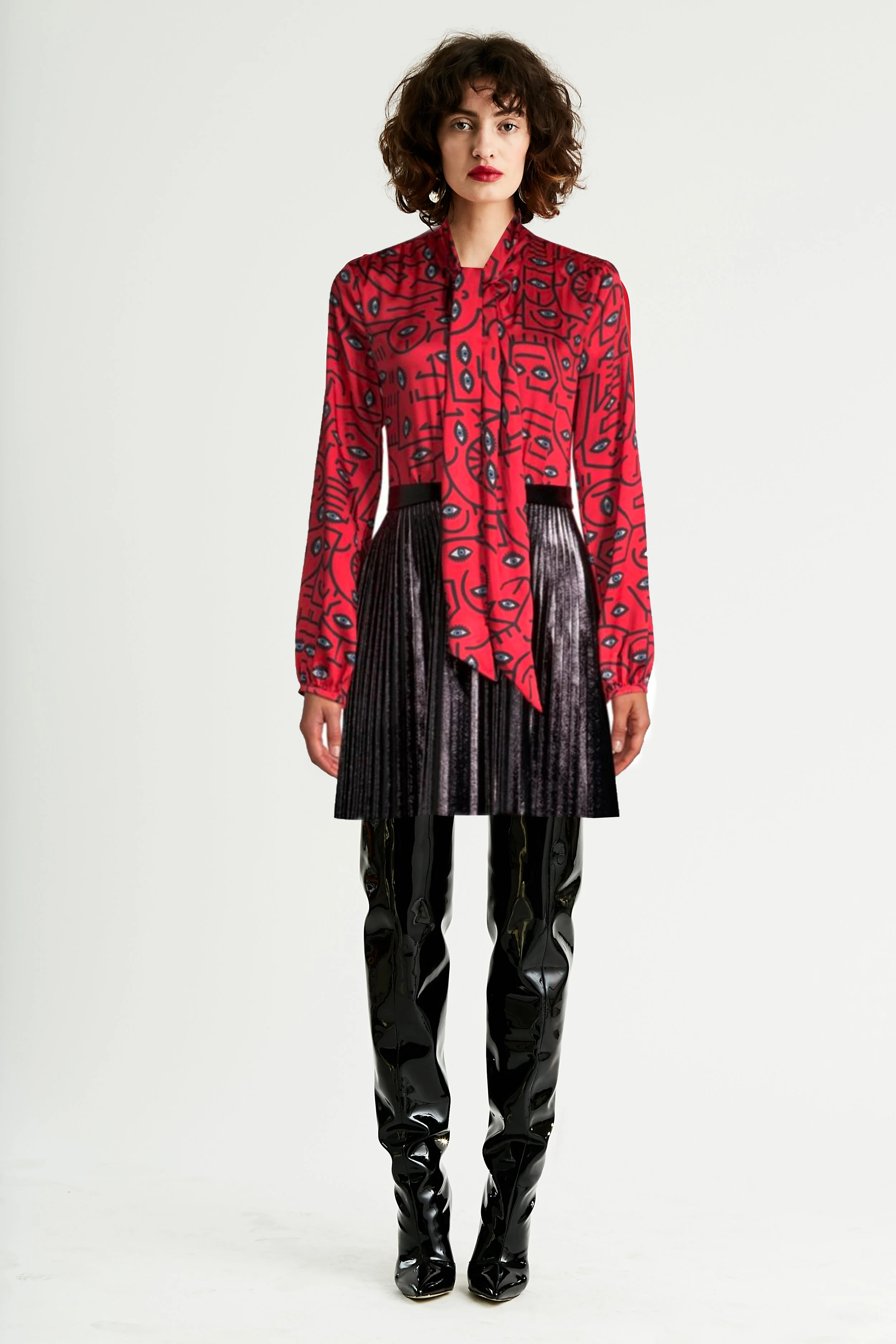 Model stands in mixed materials dress with red blouse in geometric print and skirt in faux patent leather