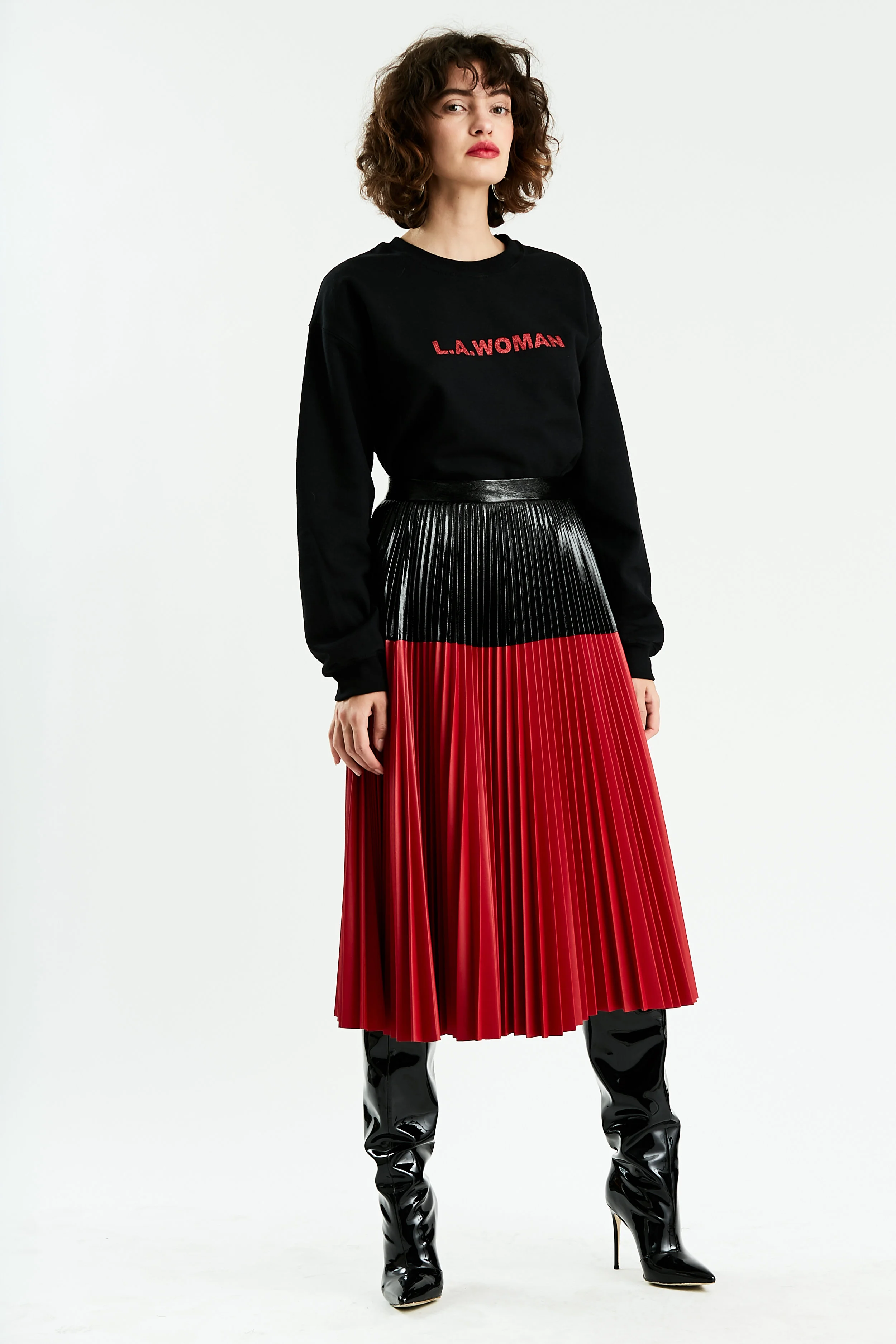 Model stands in black sweatshirt and color block faux patent leather skirt with black yoke and red hem