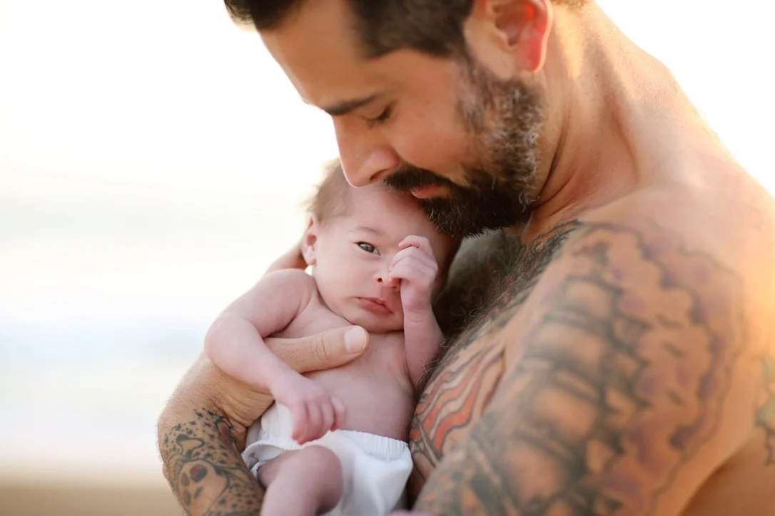 Portrait of a father holding his baby in his arms. Arms are covered in tattoos making this photo a piece of fine artististry 