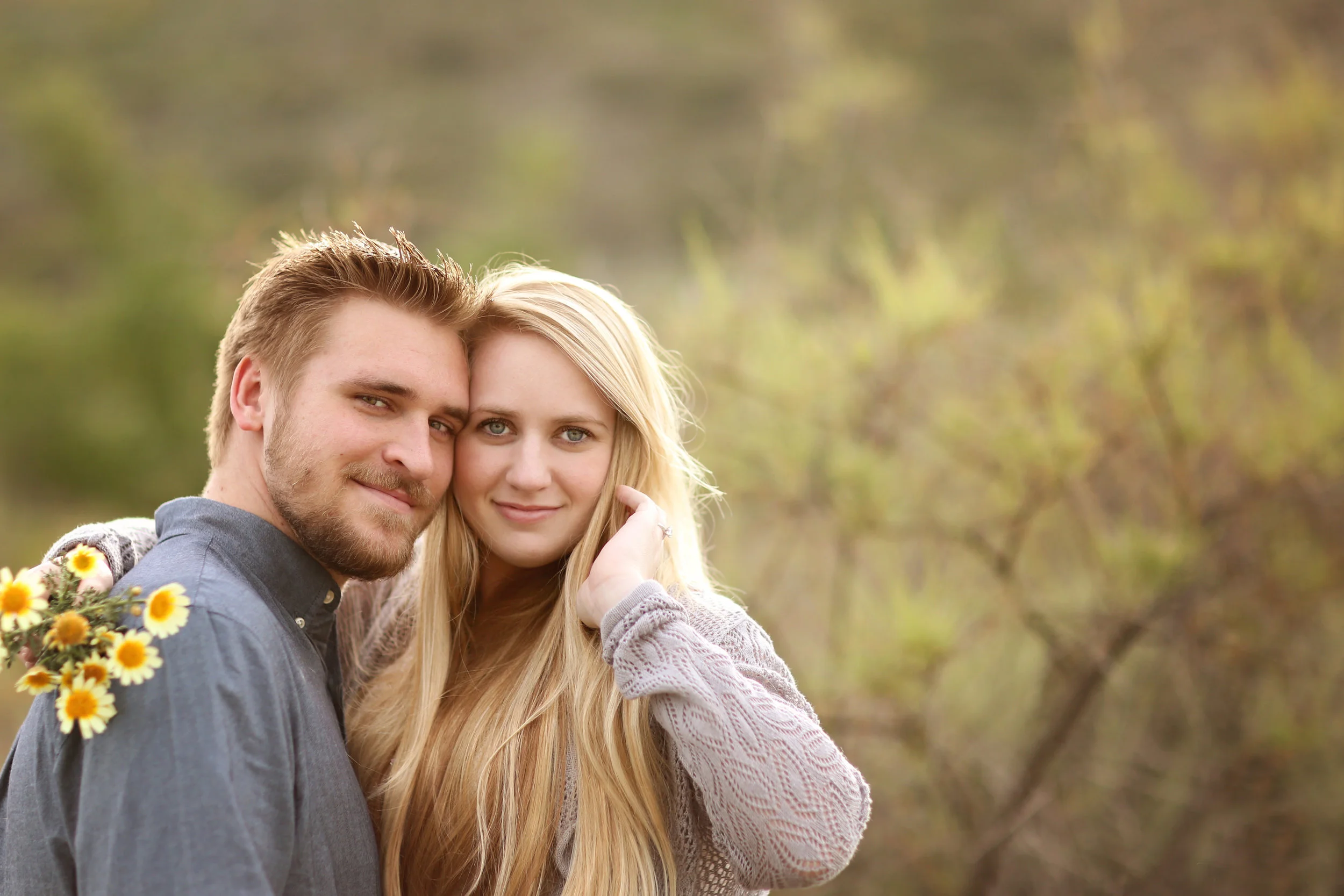 Future bride and groom in a beautiful field holding yellow flowers for their engagement photo. Orange County location.
