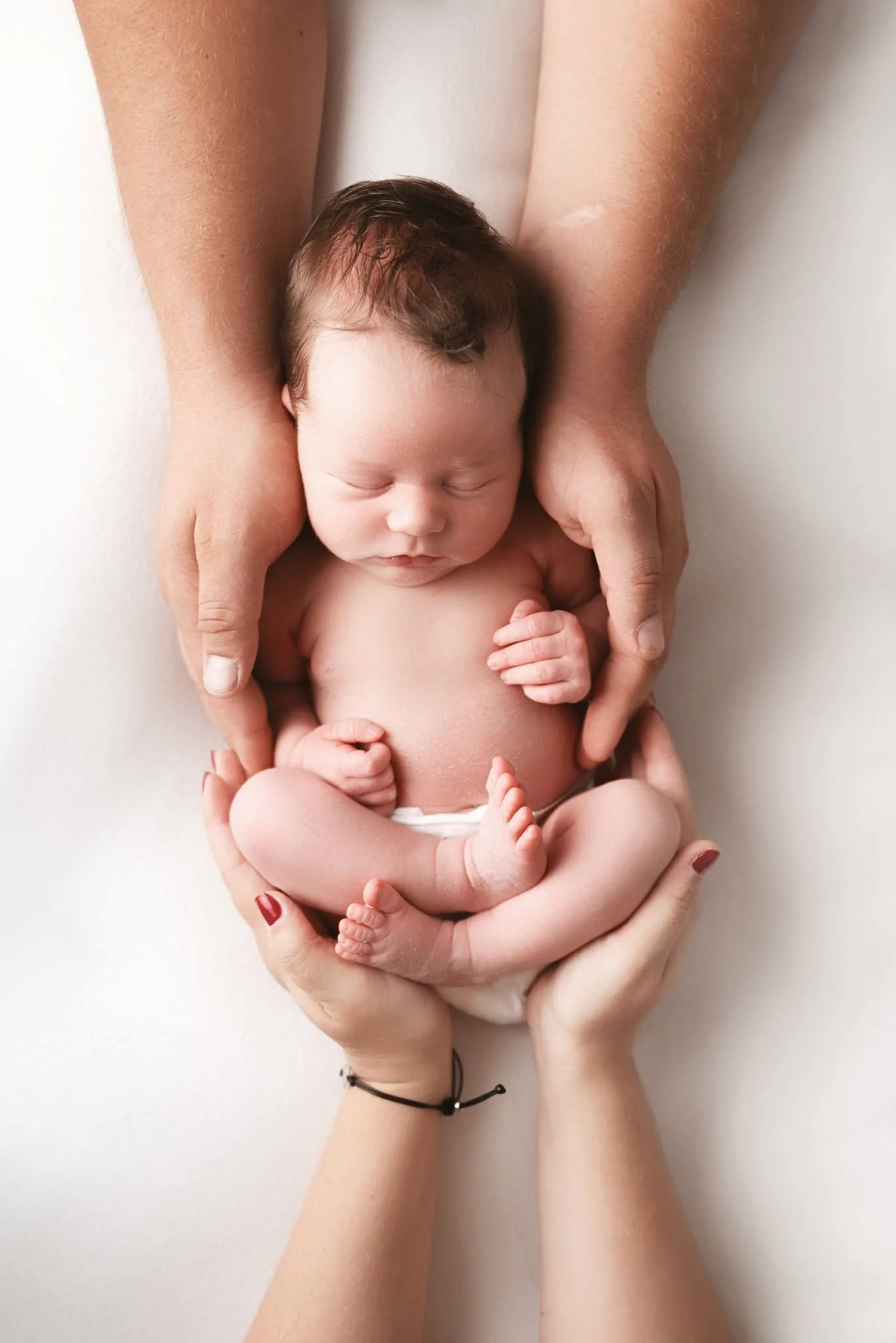 Close-up of a newborn baby sleeping, cradled in adult hands, on a white background.