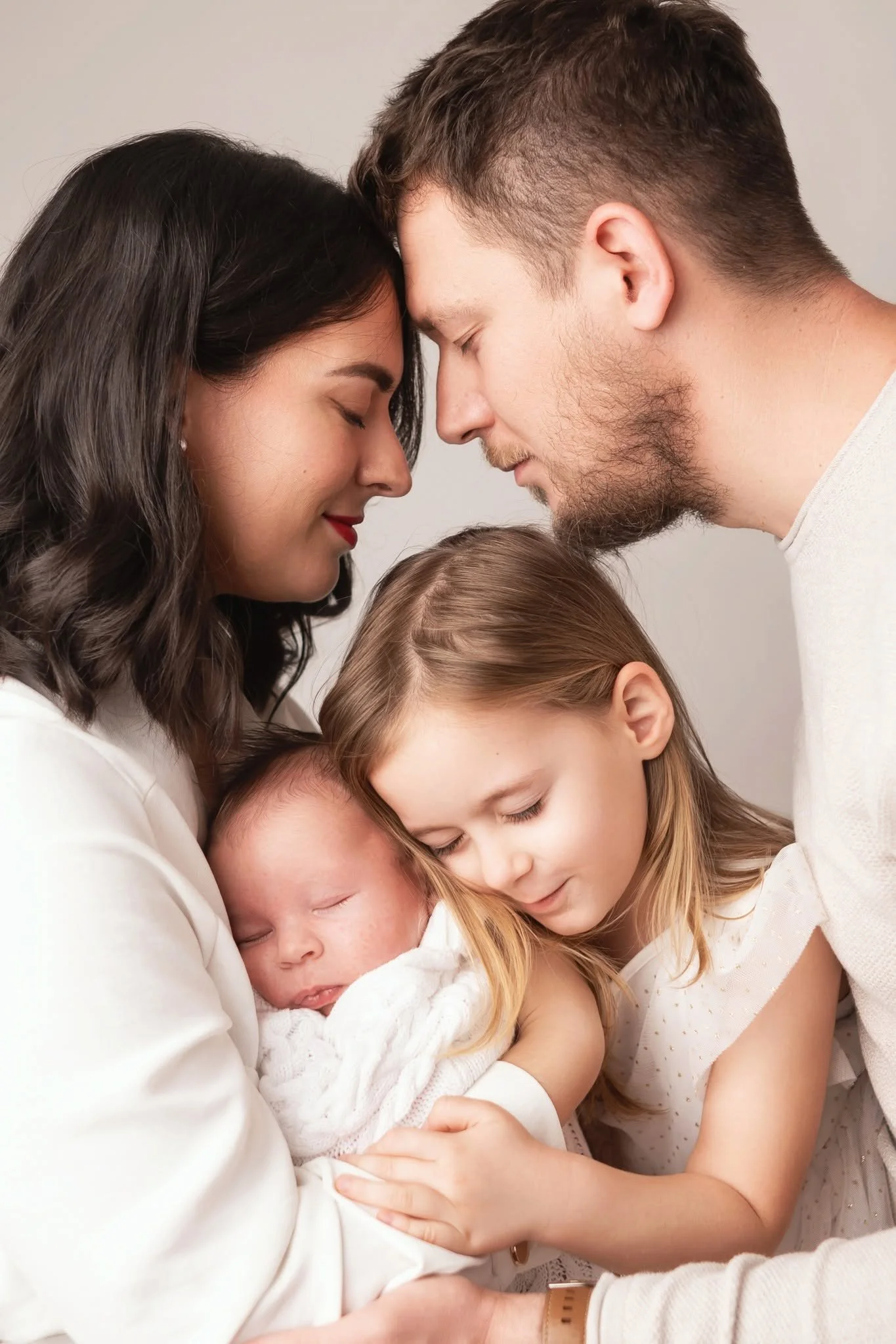 A multi-generational family of five with two parents and three children are embracing with their foreheads touching, showing love and bonding.
