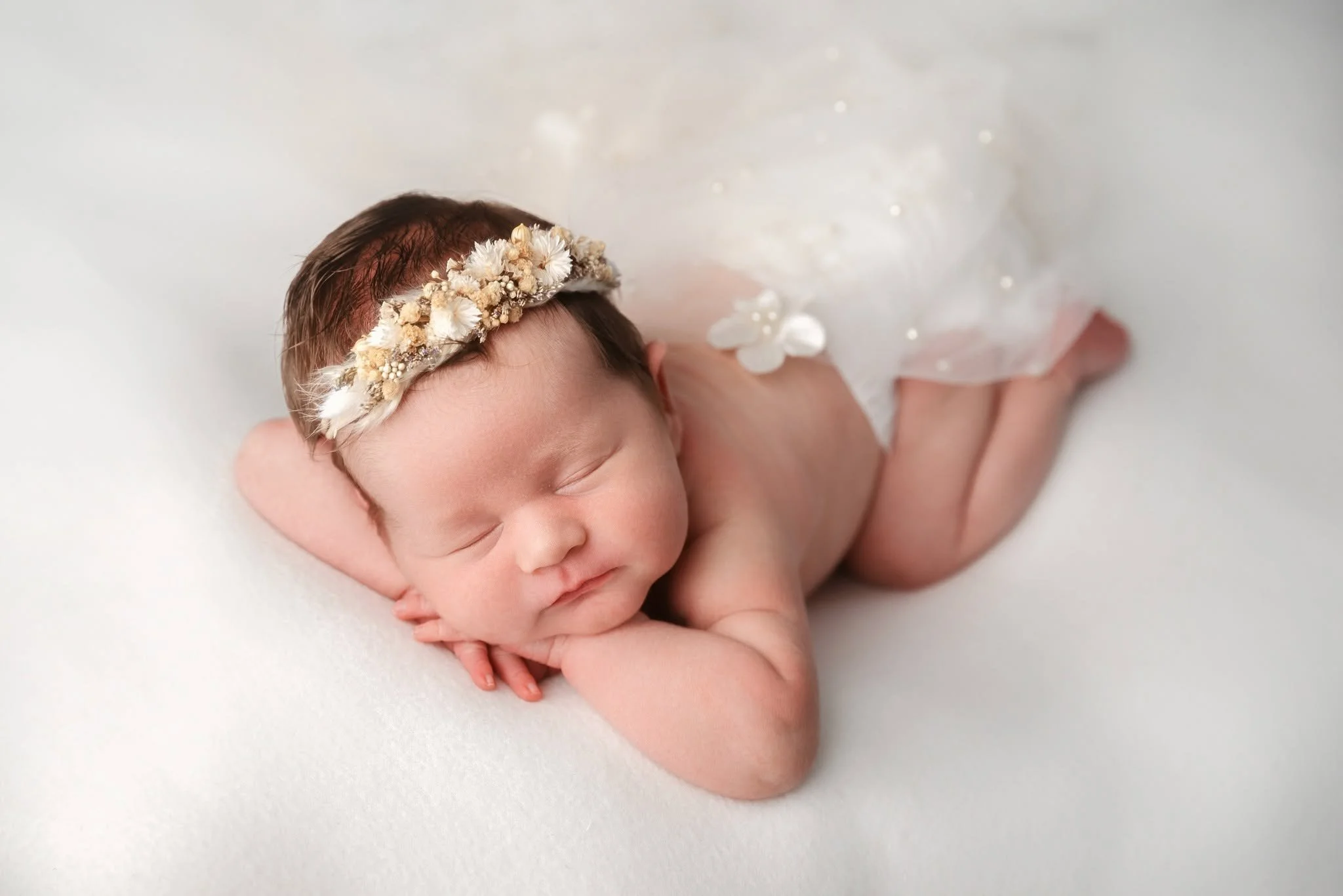 A newborn baby with a floral crown sleeping on a soft surface.