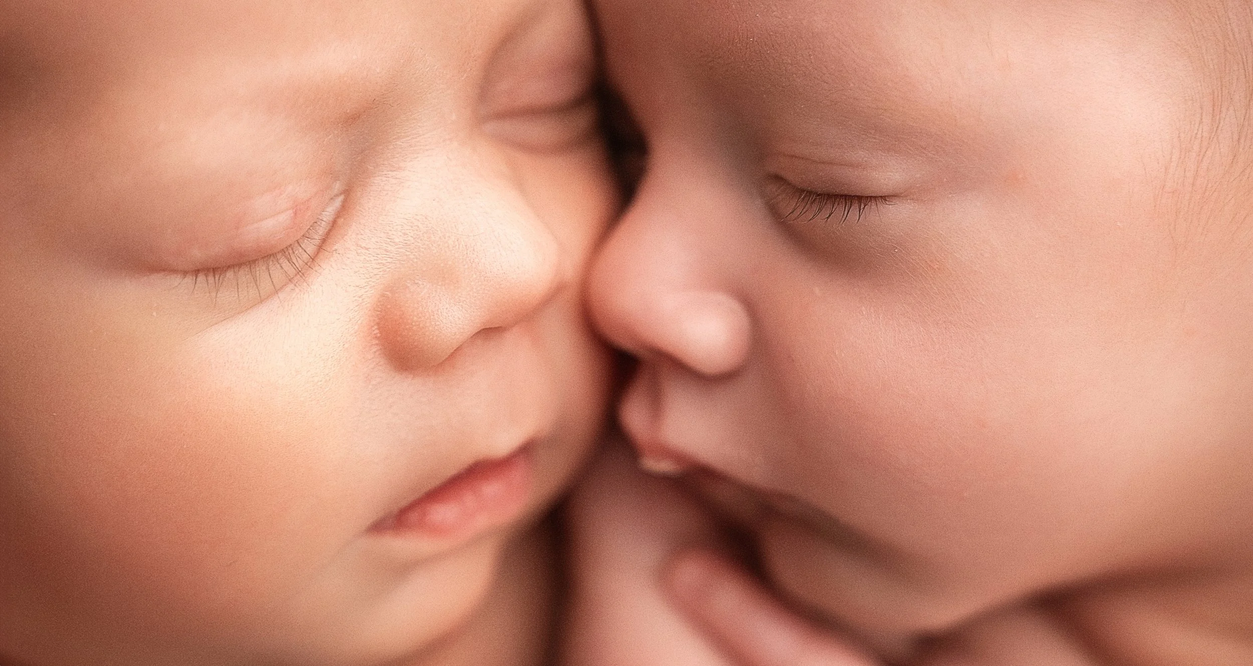 Close-up of two babies touching their noses together with closed eyes.