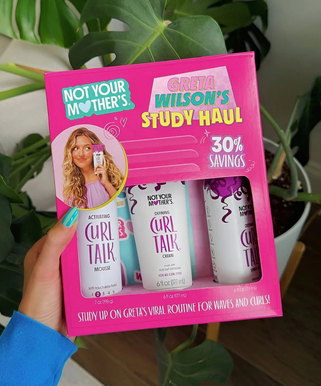 A pink box containing three curl defining products from the brand "Not Your Mother’s." The box features a woman with curly blonde hair holding a product, and text promoting a study haul with 30% savings. The products include mousse, curl defining cream, and gel, with a background of green plants.