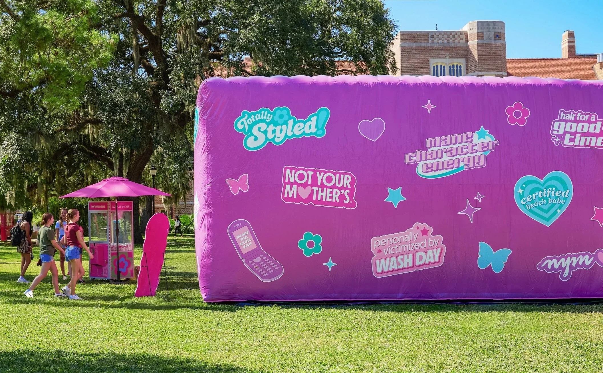 A group of young girls walking past a Y2K-inspired pink inflatable structure with love and flower prints at an outdoor event, with trees and buildings in the background at Not Your Mother's haircare college pop-up event at Florida State University