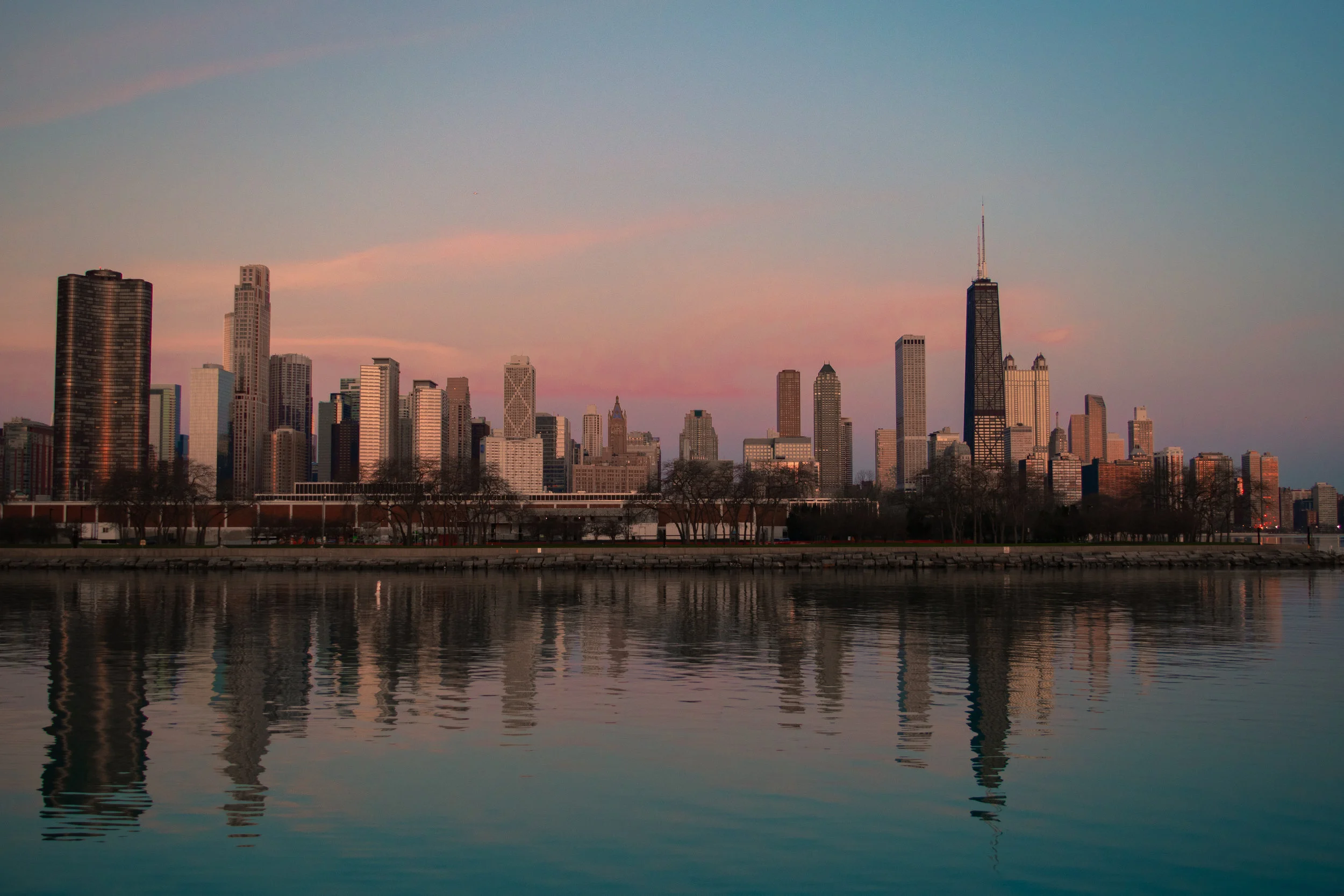 City skyline of Chicago at sunset with tall buildings reflected in the water.
