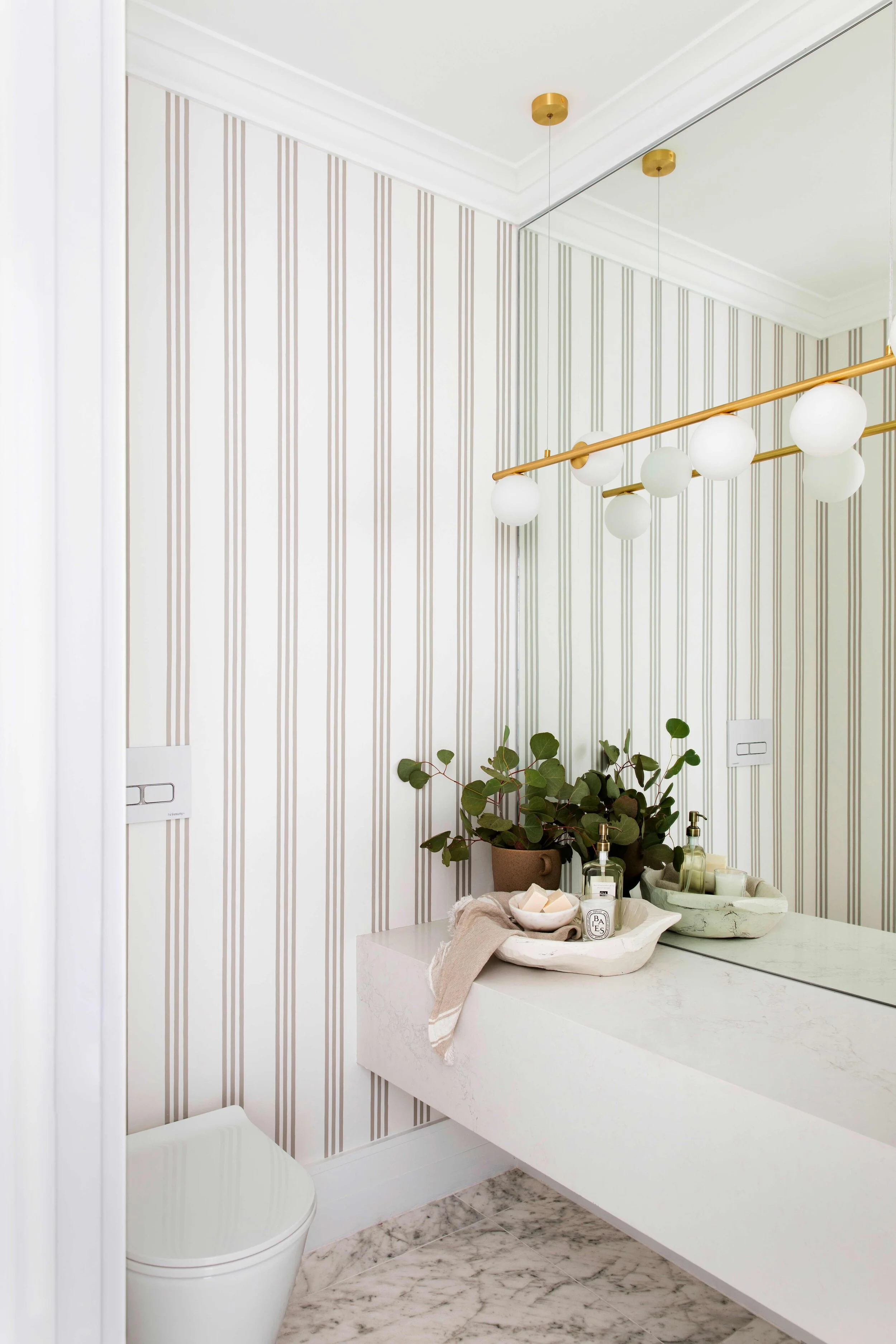 Three Birds Renovations House 14 powder room with striped wallpaper, floating stone vanity, brass globe pendant light and marble flooring.