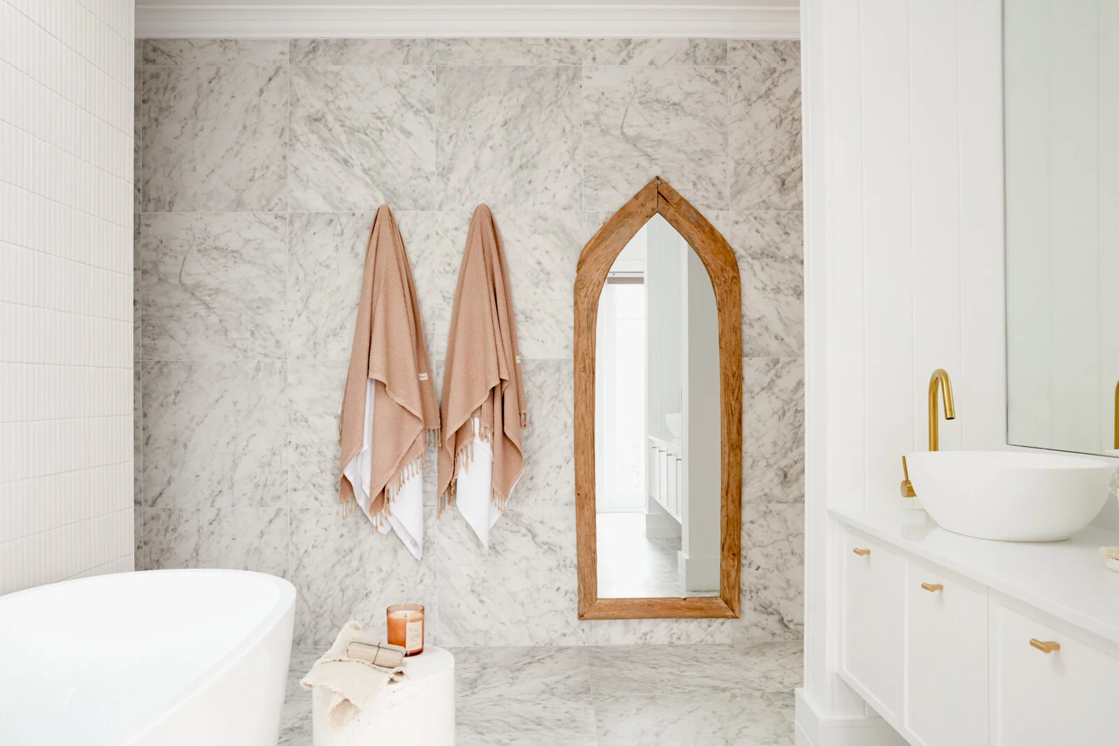 Three Birds Renovations House 14 bathroom with marble-look wall tiles, a sculptural timber mirror, blush towels and warm brass fixtures creating a luxurious retreat.