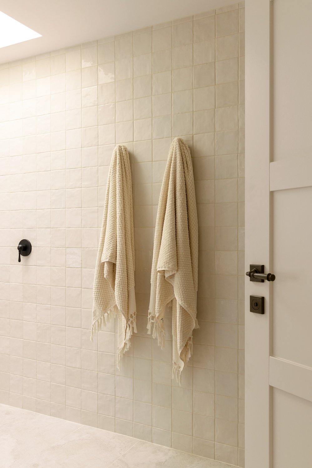 Three Birds Renovations House 16, minimalist bathroom with soft beige tiles, black fixtures, and textured towels creating a calm, spa-like atmosphere with modern coastal elegance.