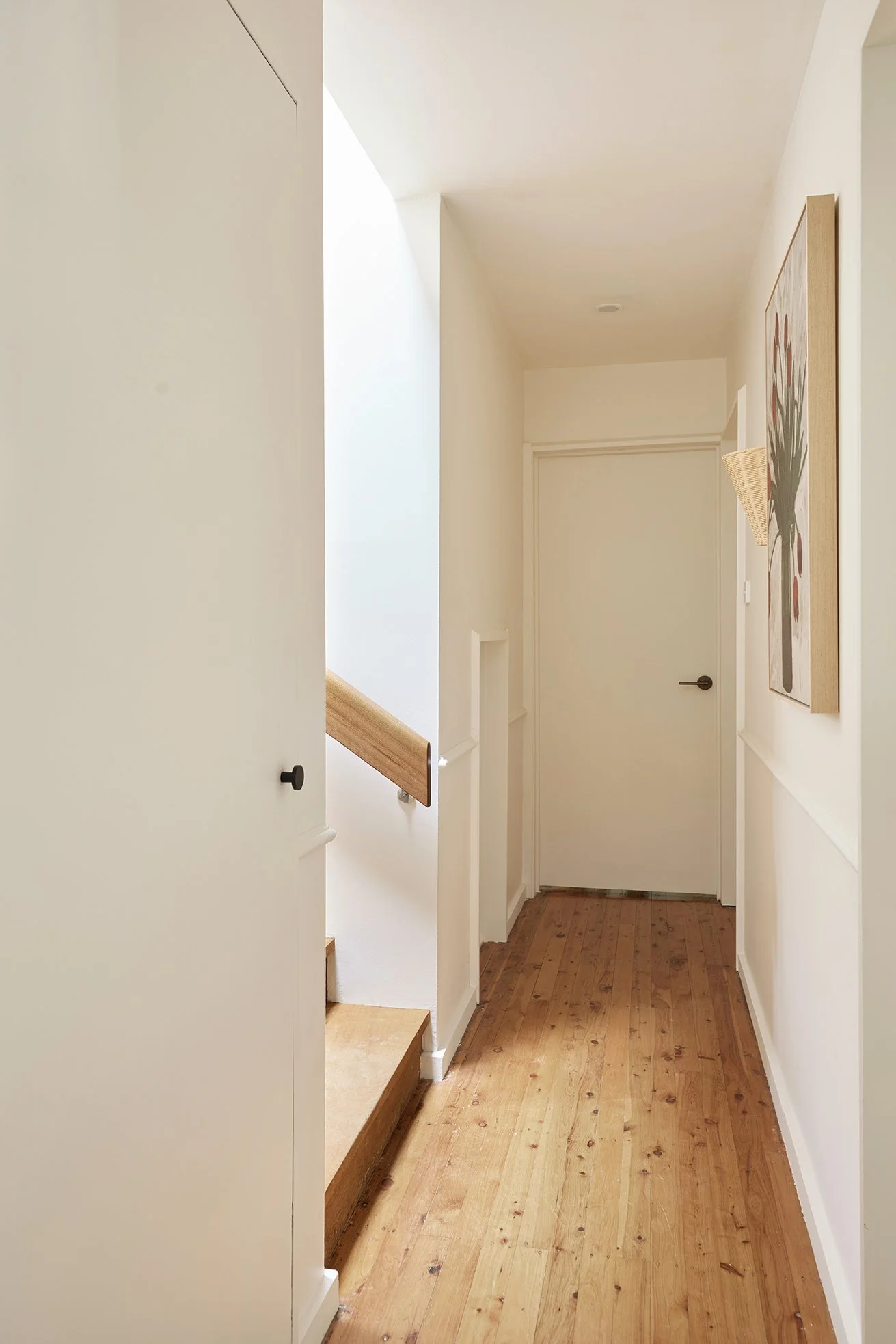 Three Birds Renovations Hallway Transformation with timber floors, white walls, tulip artwork and woven wall sconce.