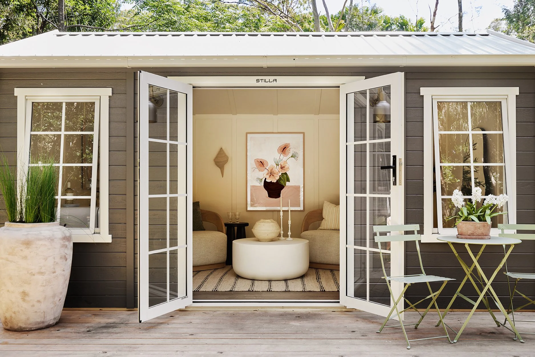 Three Birds Renovations Eclectic Escape garden studio with French doors, cosy seating, soft neutral styling and a timber outdoor deck.