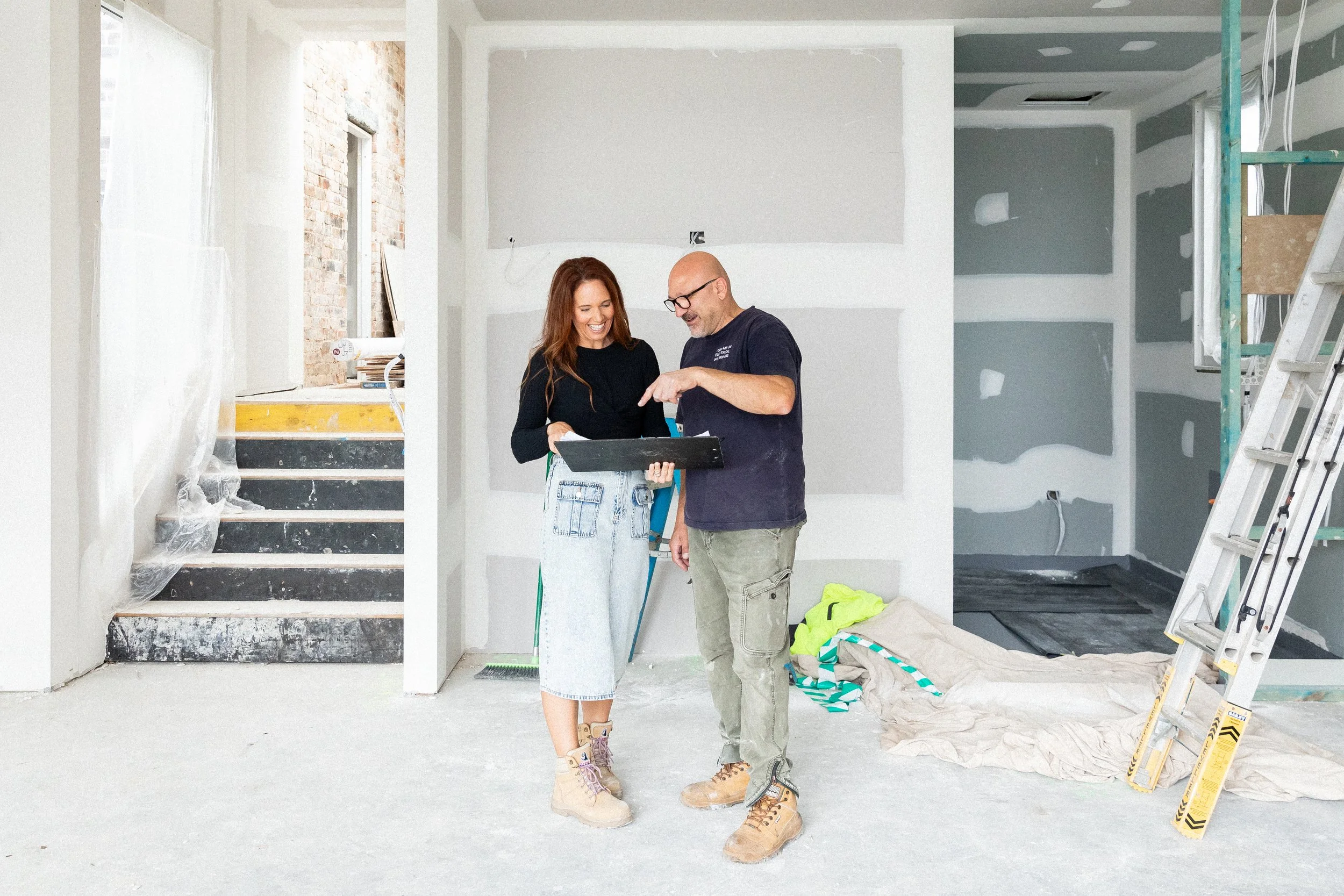Three Birds Renovations House 17 mid renovation with the Three Birds team reviewing plans on site inside a partially completed home with plasterboard, ladders and unfinished interiors.
