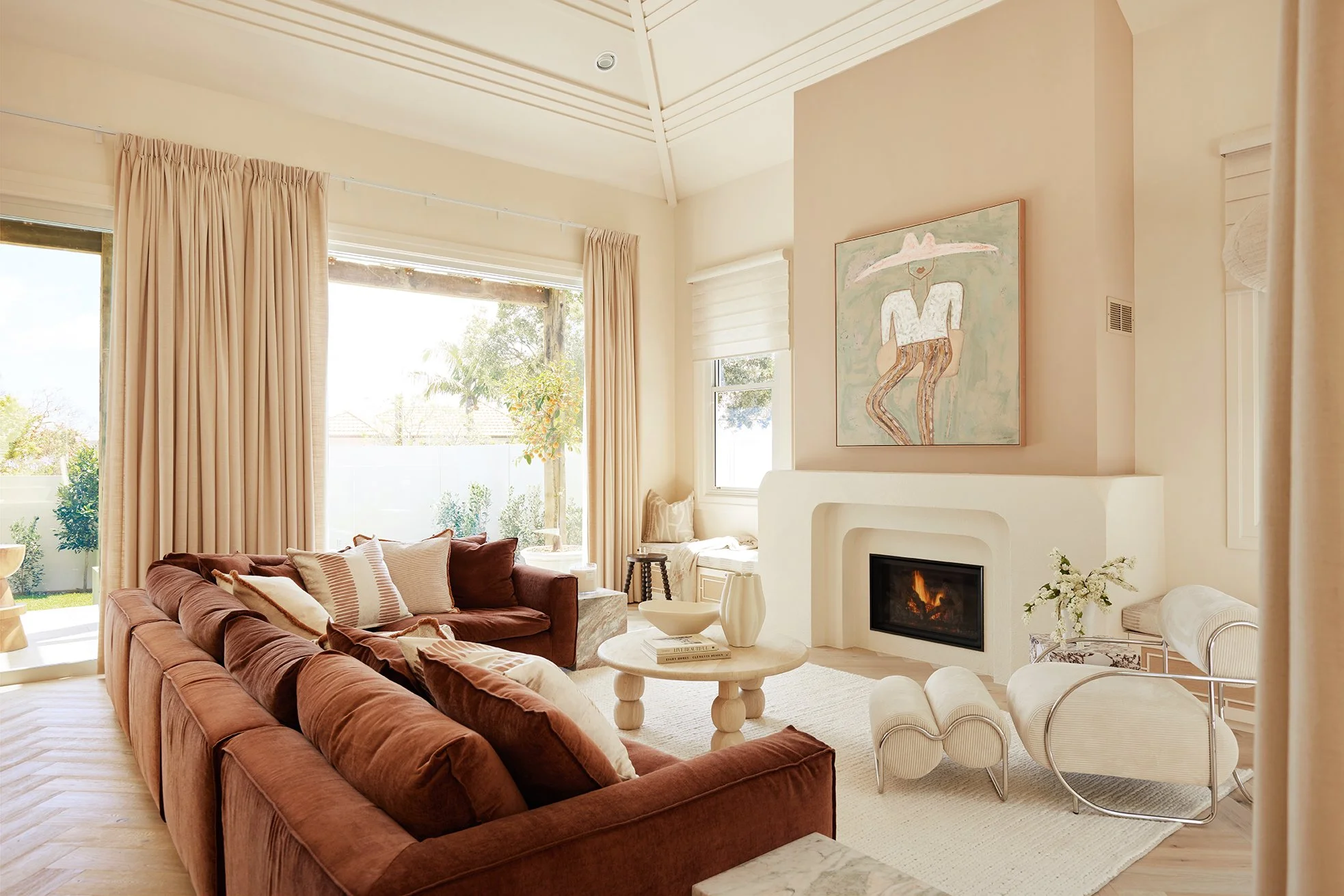 Three Birds Renovations House 17 living room with rust sectional sofa, sculptural fireplace, curved furniture and soft neutral styling opening to a sunlit garden.