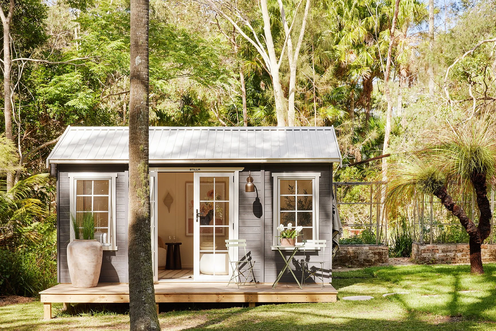 Three Birds Renovations Eclectic Escape backyard studio with dark exterior cladding, timber deck and lush tropical landscaping creating a peaceful retreat.