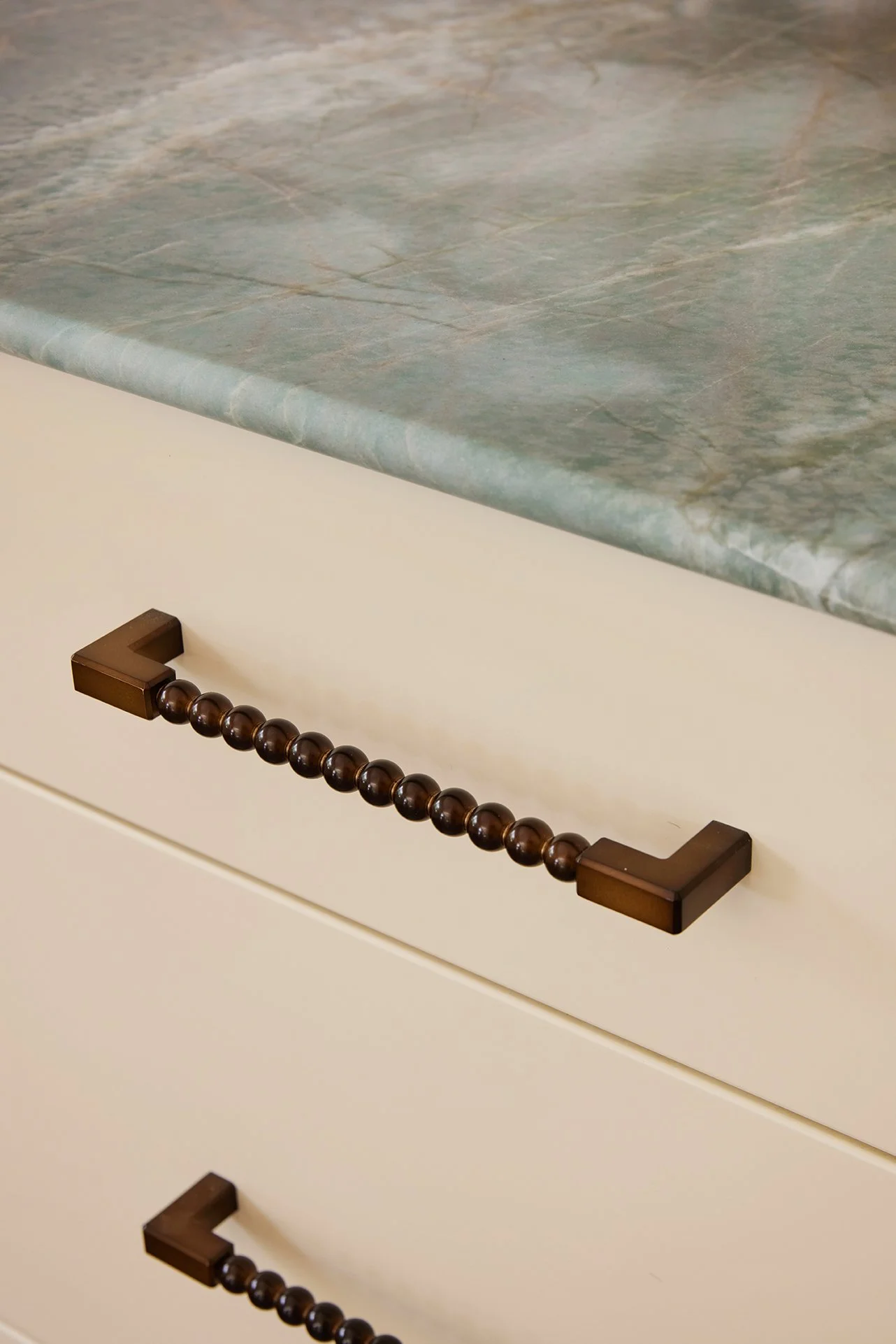 Three Birds Renovations Eclectic Escape kitchen detail with terracotta square tiles, green marble benchtop, brass hardware and decorative wall sconce.