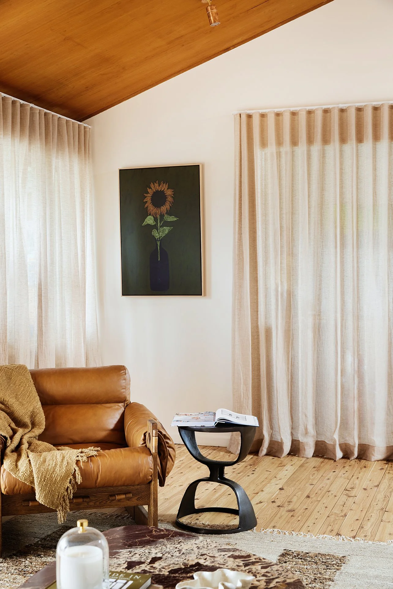 Three Birds Renovations Living Room Transformation with leather armchair, sculptural side table, linen curtains and sunflower artwork.