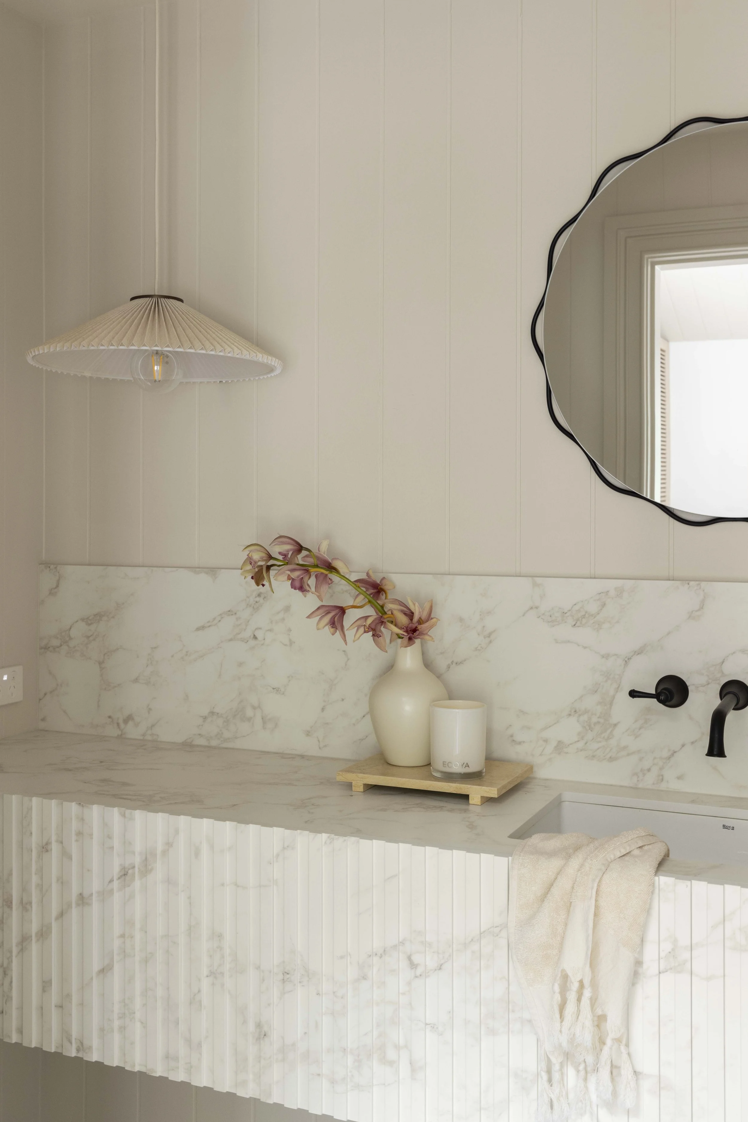 Three Birds Renovations House 16 bathroom with marble vanity, fluted detailing, black wall tapware and soft styling with orchid stems and candle.