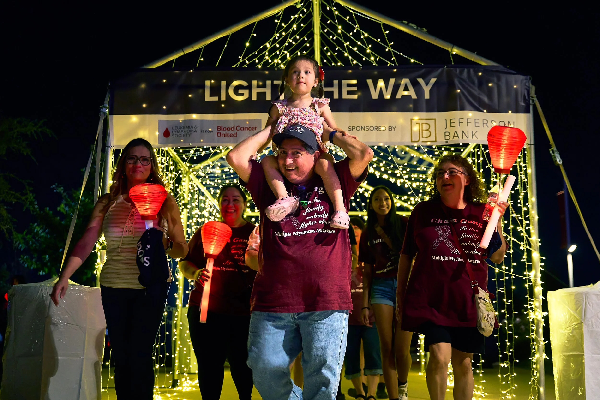 Family participating in a Leukemia and Lymphoma Society Light the Way charity walk at night in San Antonio.