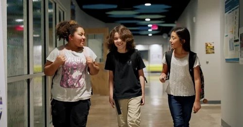 Diverse students walking and talking happily in a brightly lit school hallway for educational content.