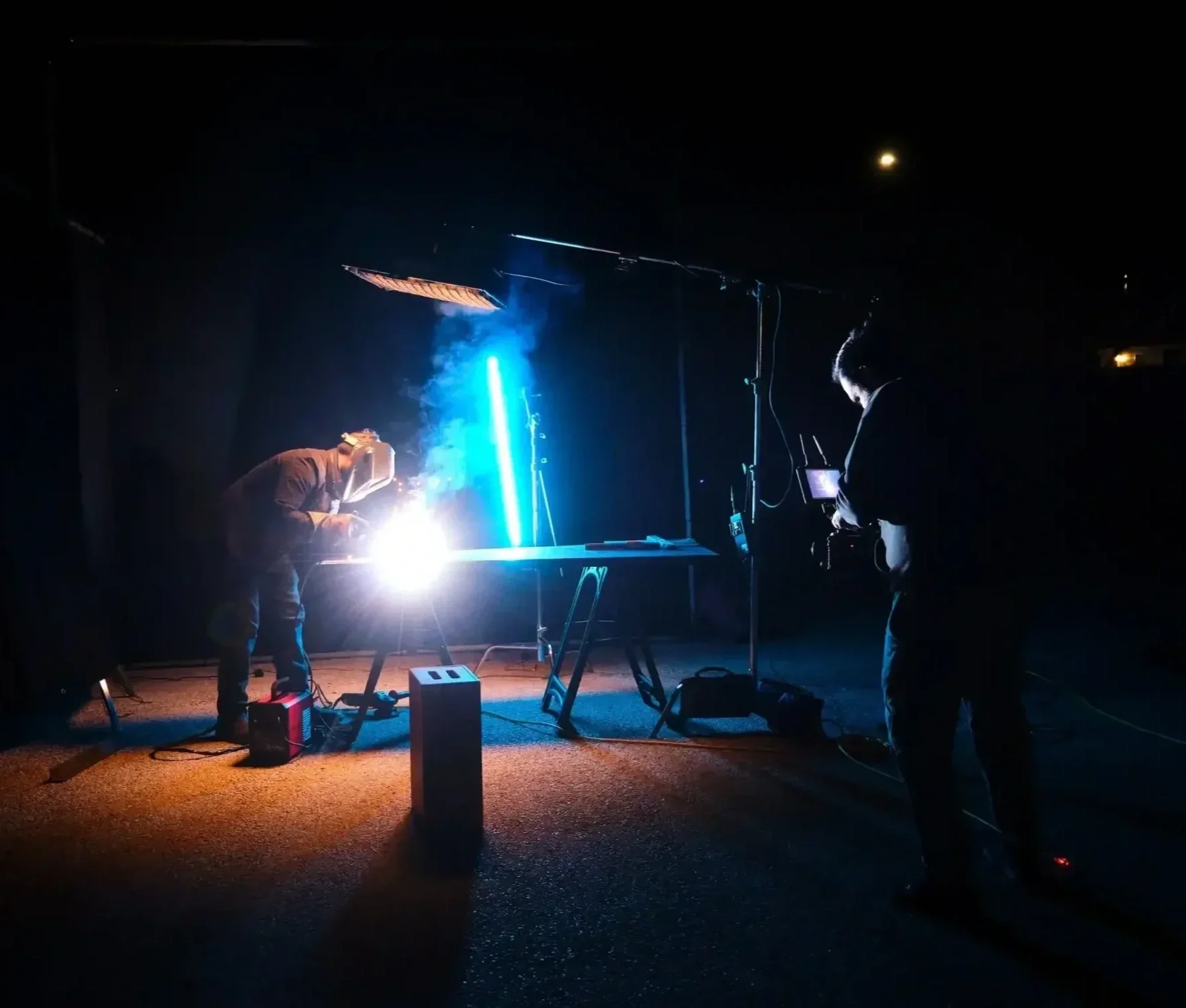 Film crew capturing a welding scene with dramatic blue and orange lighting during a commercial video production.