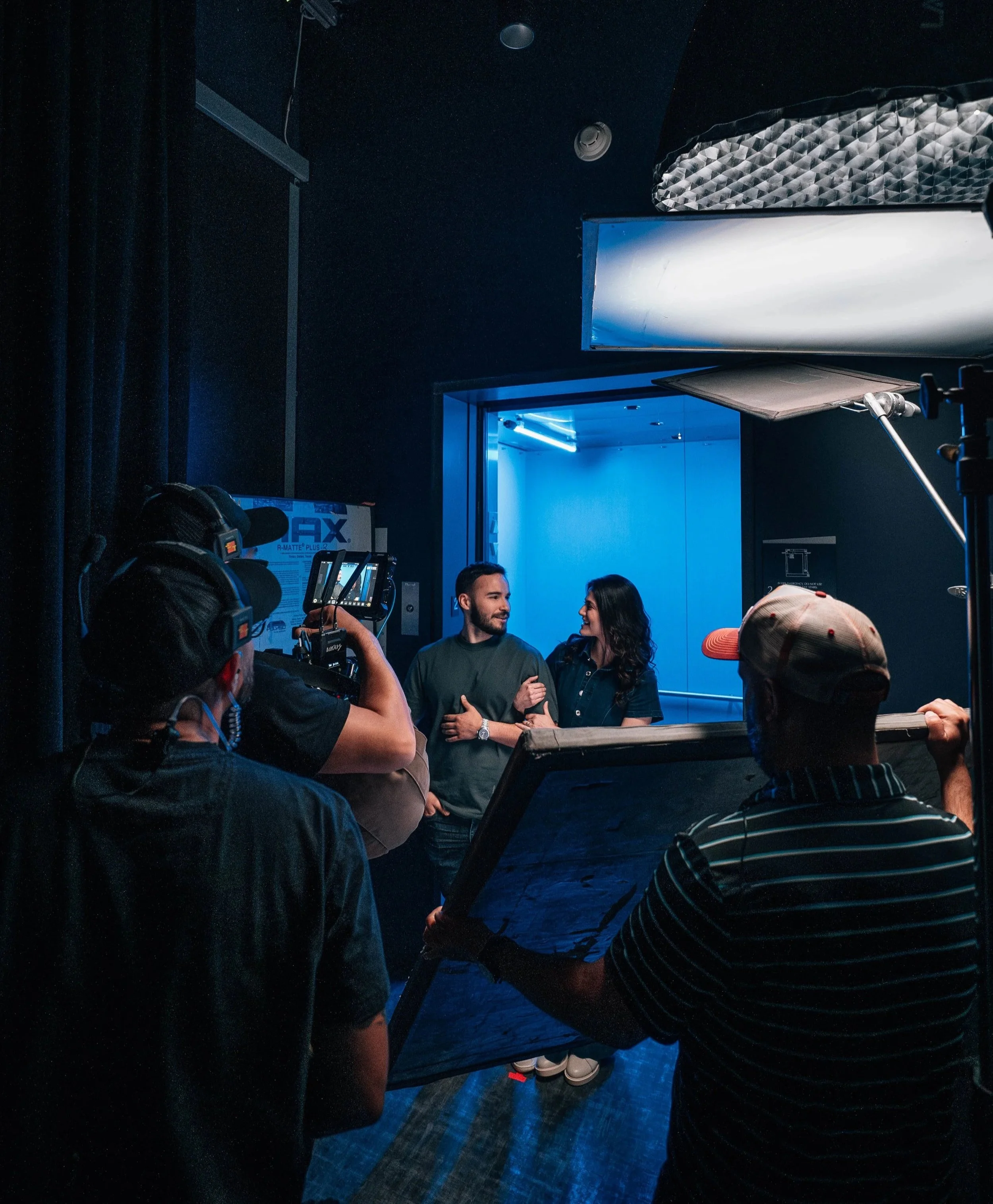 Film crew shooting a two person interview scene with professional lighting during a commercial video production.