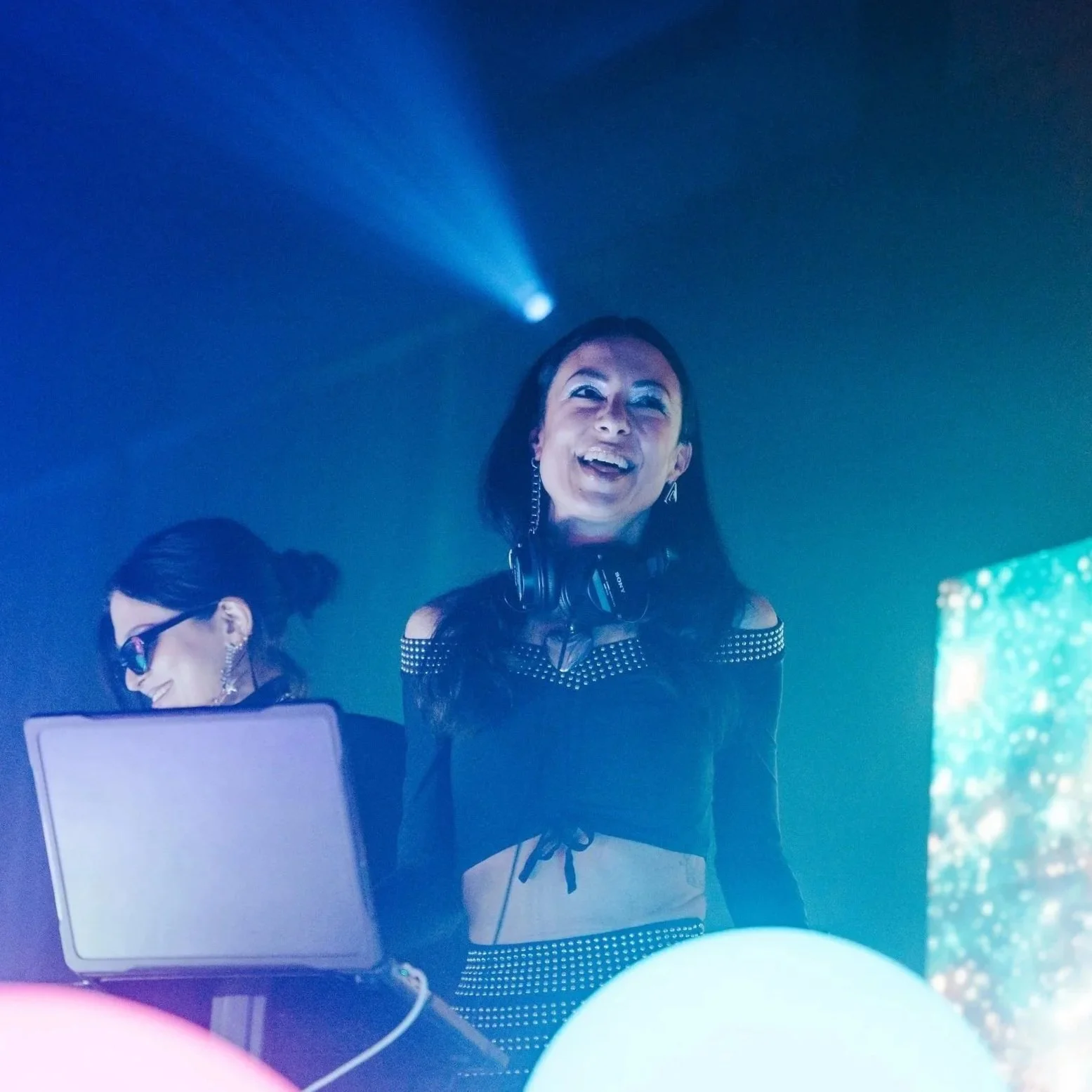 Female DJ performing under blue stage lights with headphones at a live entertainment event.