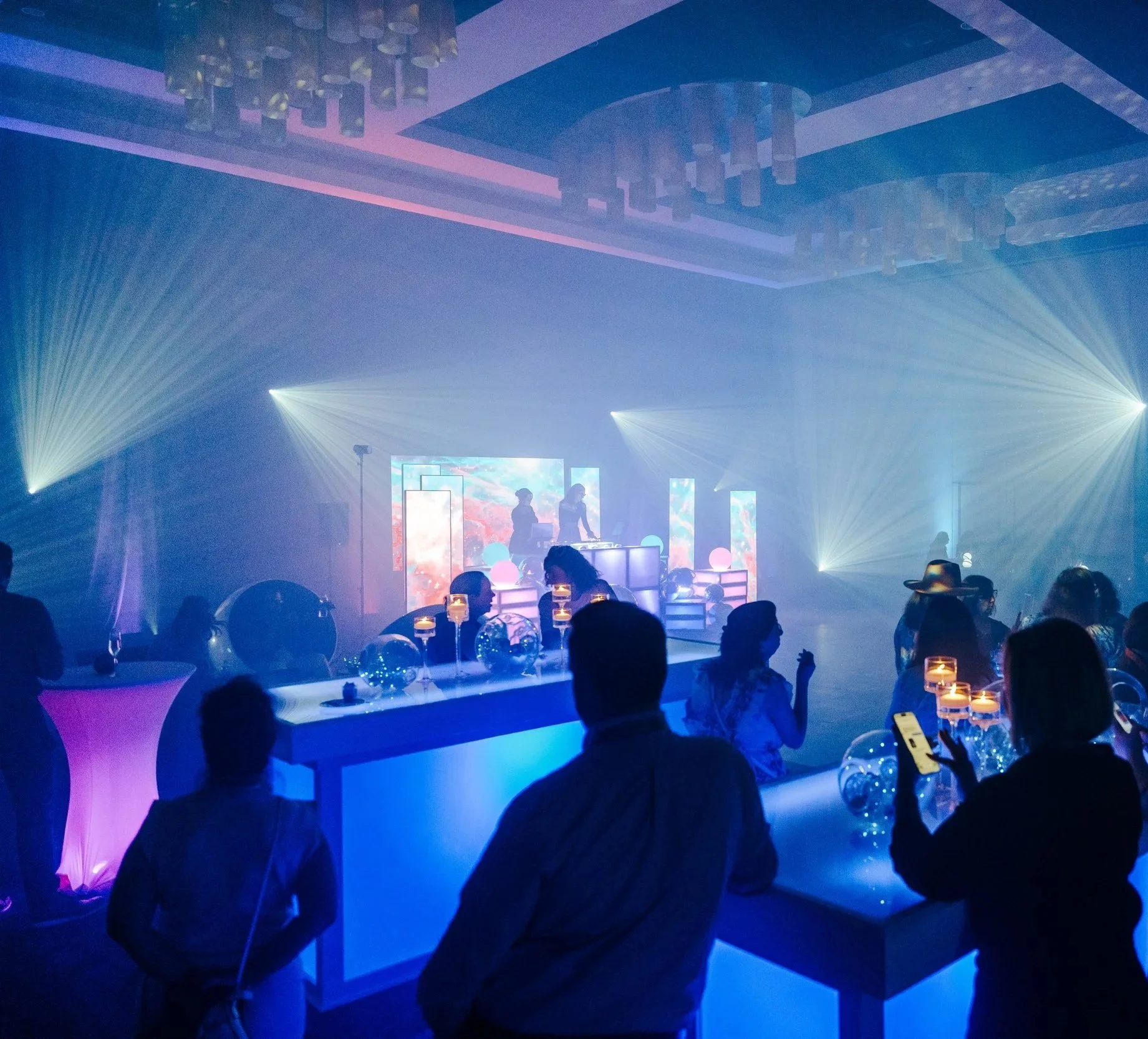 Silhouetted crowd dancing under stage lights at a live indoor corporate entertainment event.