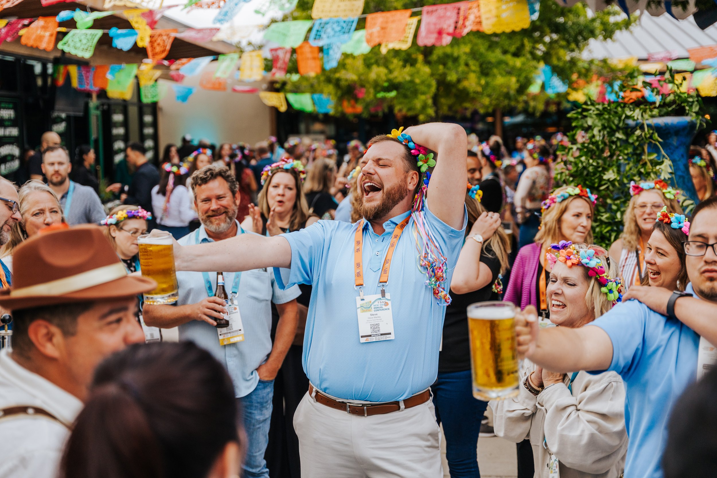 Crowd celebrating at a colorful outdoor corporate event with papel picado and beer in San Antonio.