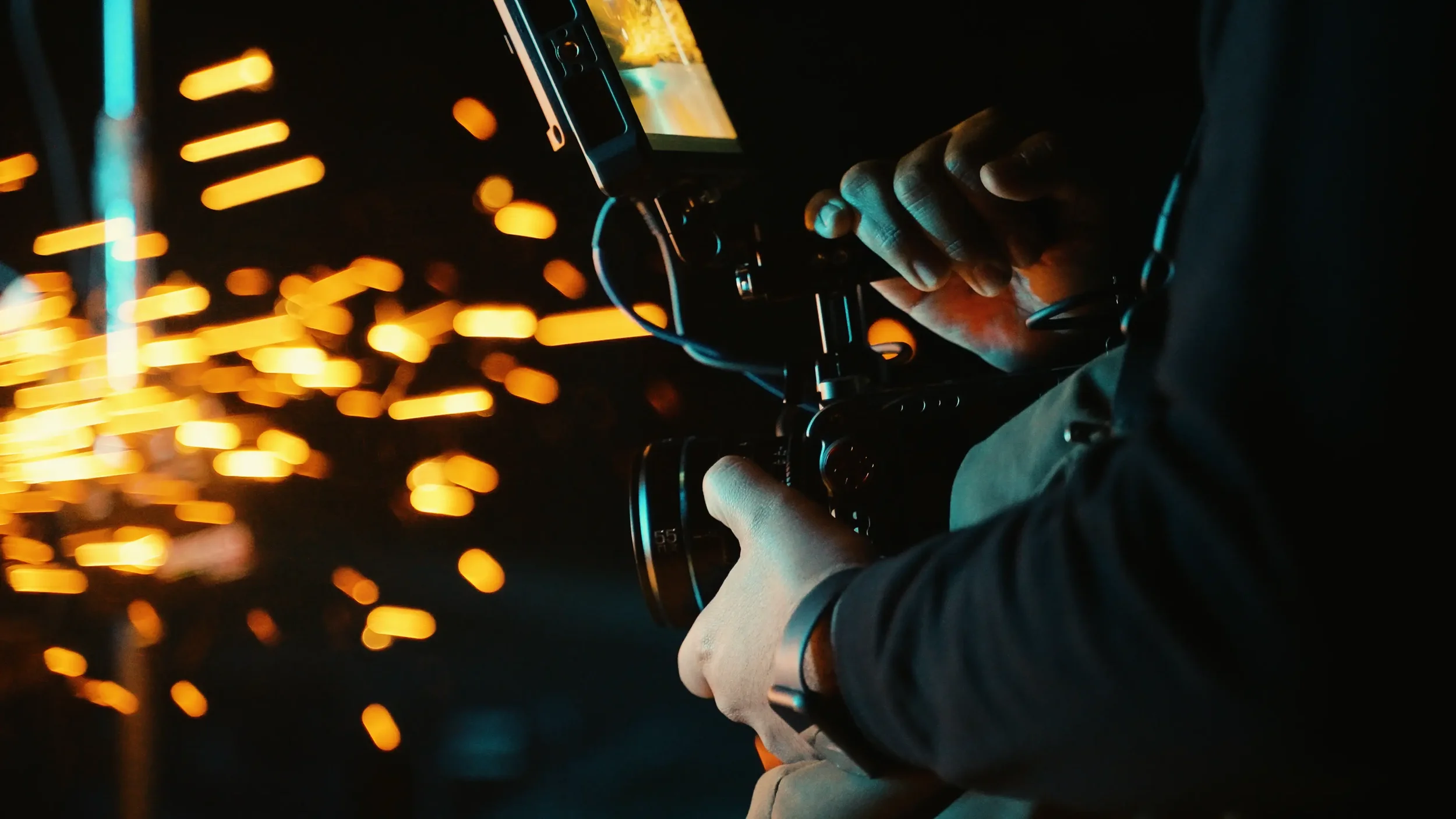 Videographer operating a camera gimbal with golden bokeh sparks during a cinematic commercial production.