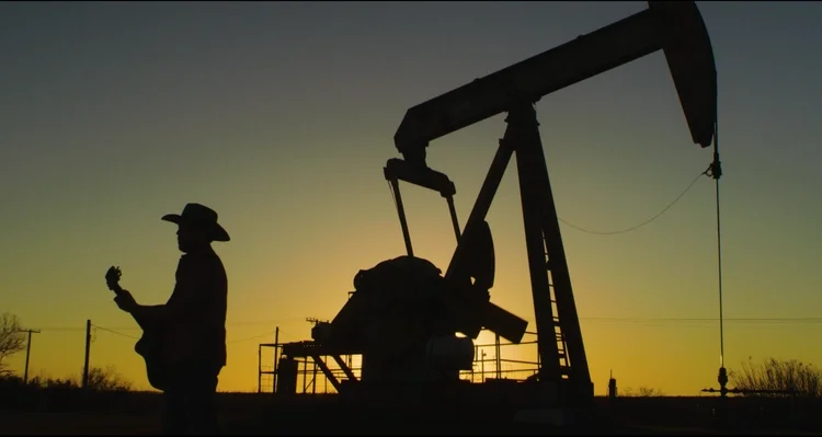 Silhouette of Kyle Park playing guitar in front of an oil pump jack at sunset for the country music video.