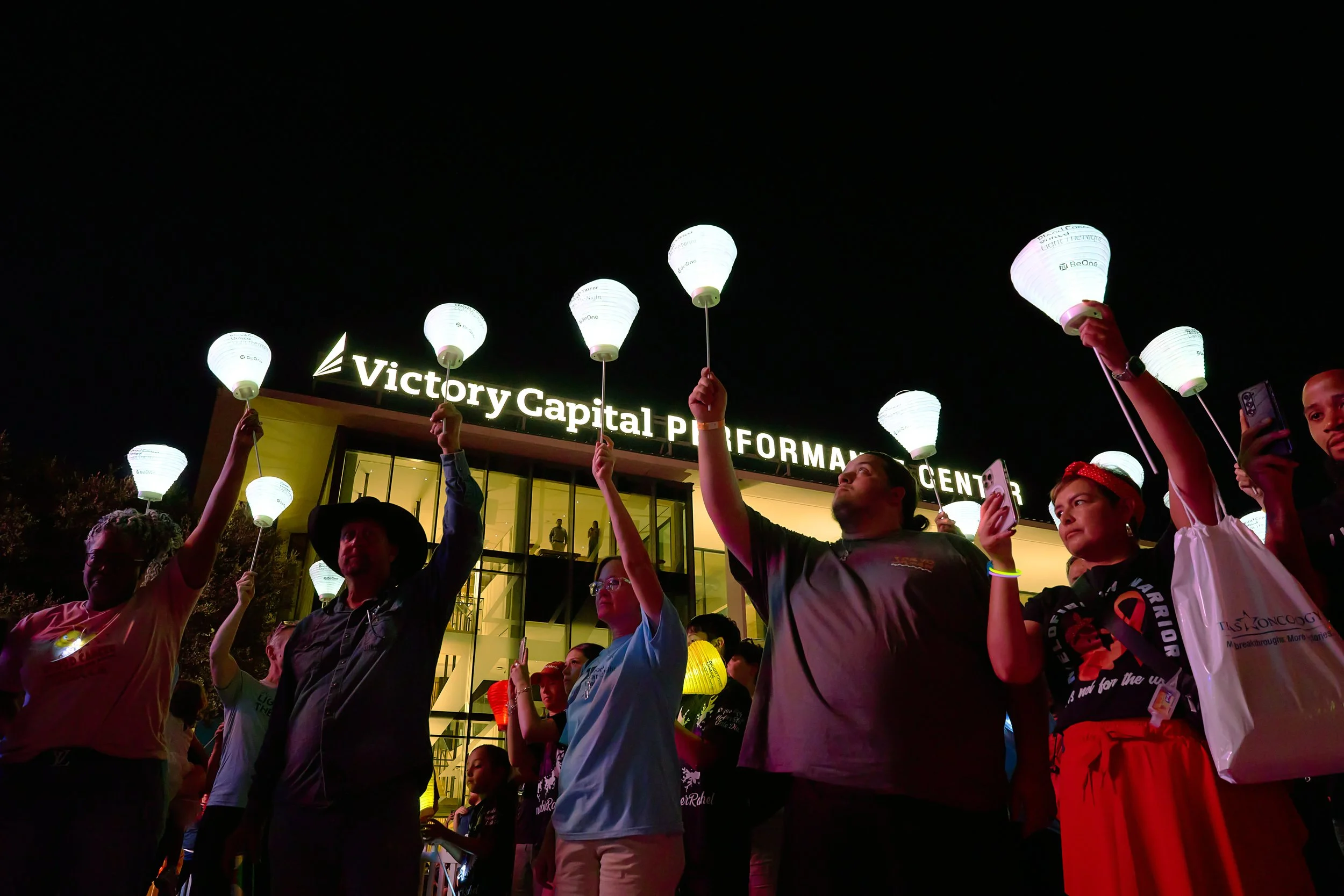 Crowd holding glowing lanterns outside Victory Capital Performance Center at a nighttime San Antonio event.