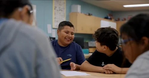 Middle school students working on a science or education activity at a table in a classroom.