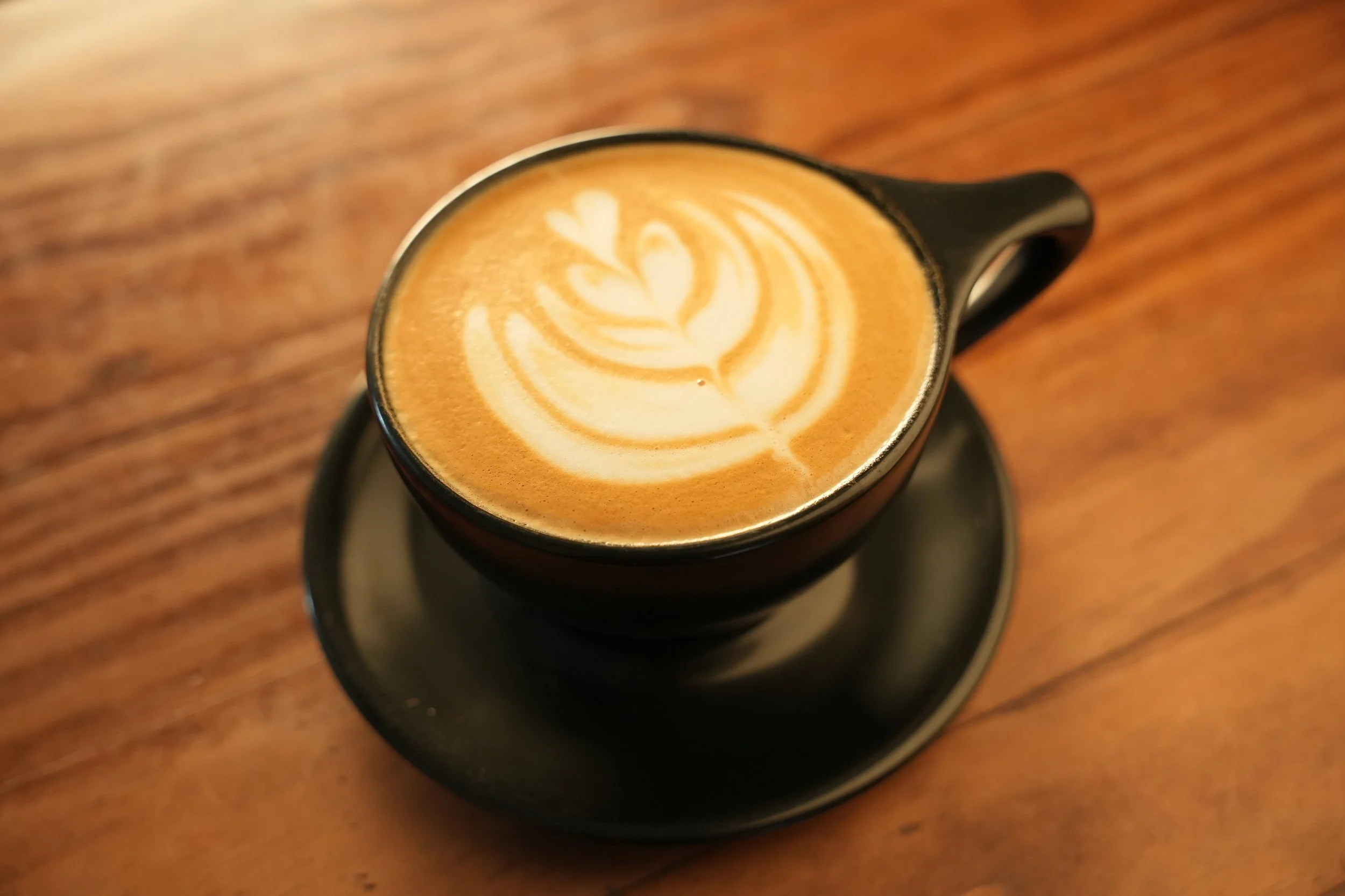 Latte with tulip milk foam art in a black ceramic cup for cafe and coffee shop commercial photography.