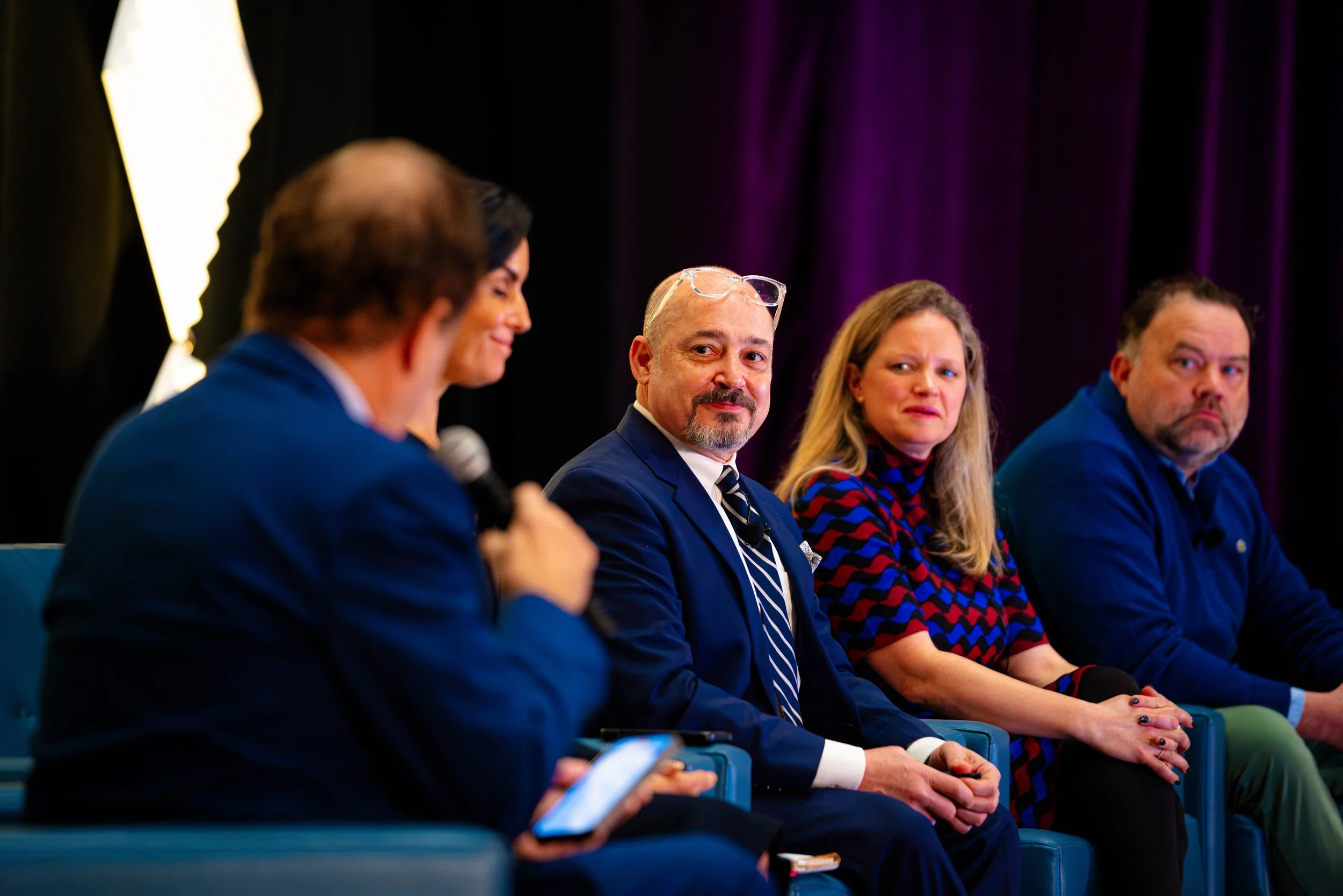 Professional panel discussion with four speakers seated on stage at a corporate conference event.