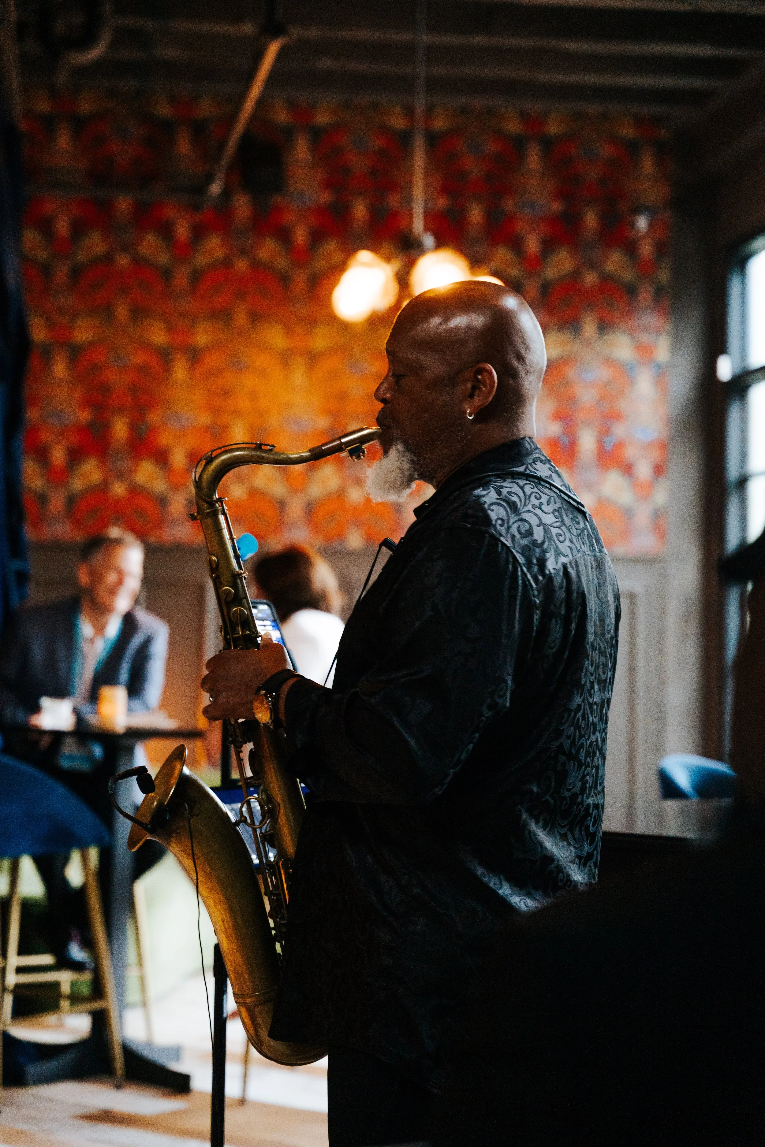 Jazz musician playing saxophone at an intimate upscale indoor dining and entertainment event.