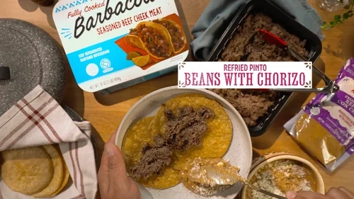 H-E-B Mi Tienda beans with chorizo product displayed on a table around other food items.