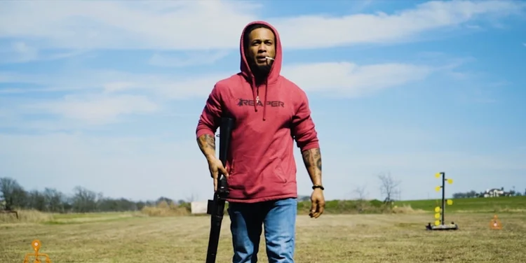 Man in a red Reaper hoodie walking through a field, a scene from the Granger Smith Holler music video.