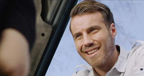 Kyle Park smiling while working under the hood of a car in the music video.