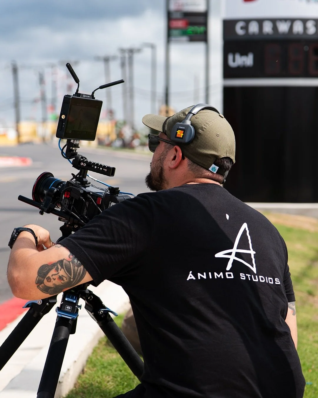 Videographer operating a cinema camera on a tripod at an outdoor commercial production shoot.