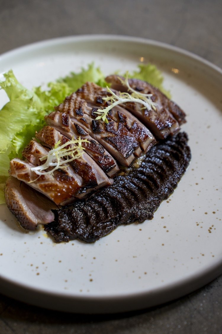 Sliced cooked duck breast with crispy skin, garnished with microgreens, served on a plate with lettuce and a black bean puree at Ubud's Best Indonesian restaurant.