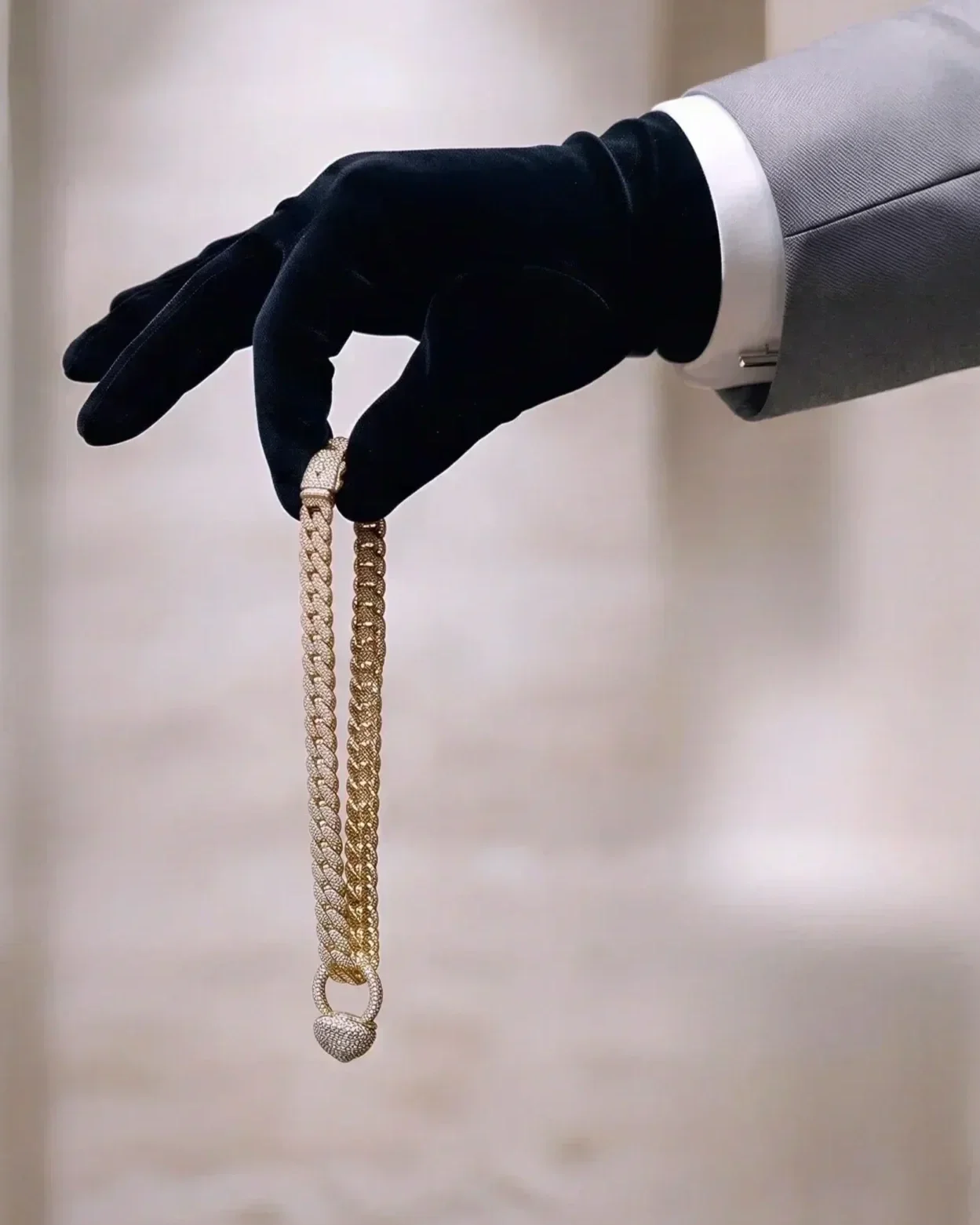 Hand wearing a black glove holding a gold chain necklace with a heart-shaped pendant.